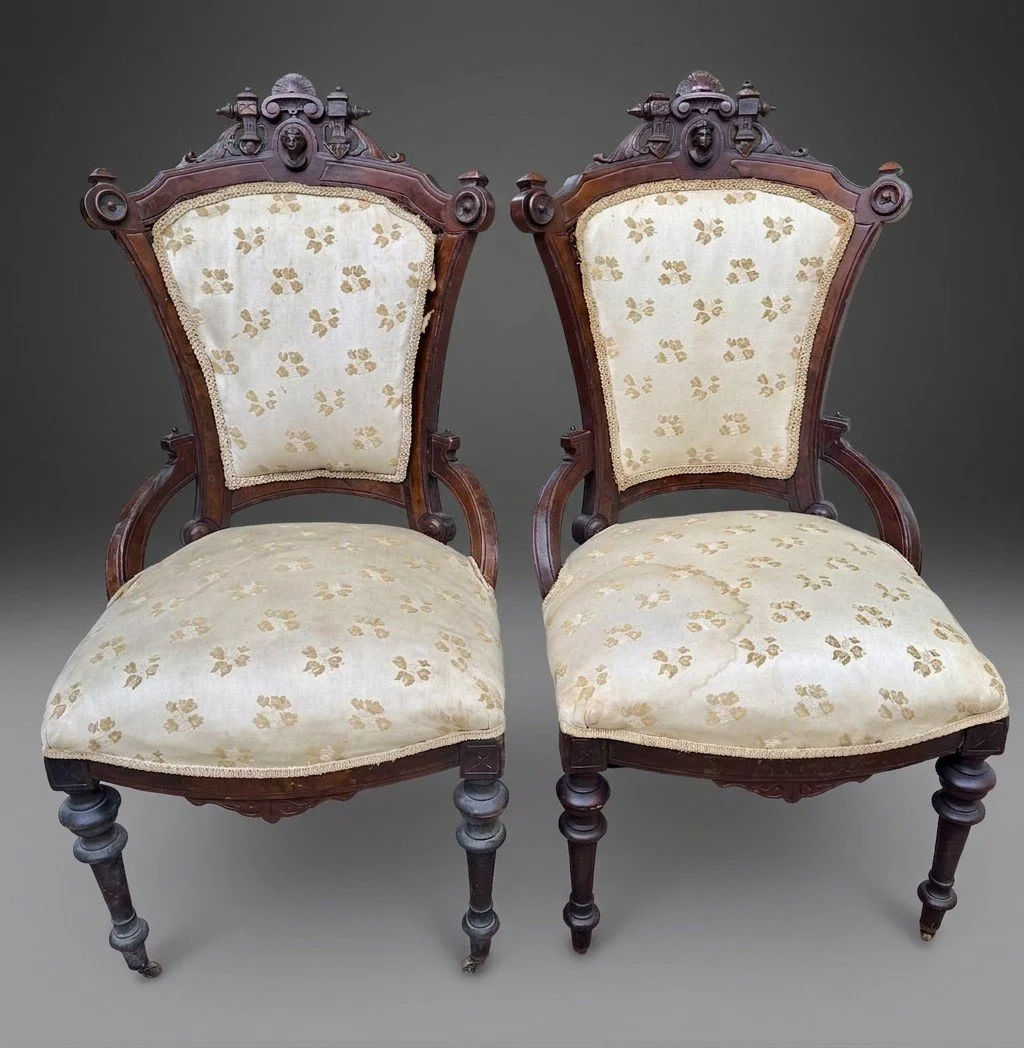 The matched pair of walnut portrait medallion chairs before restoration, in the original cream silk woven with small gold floral sprigs