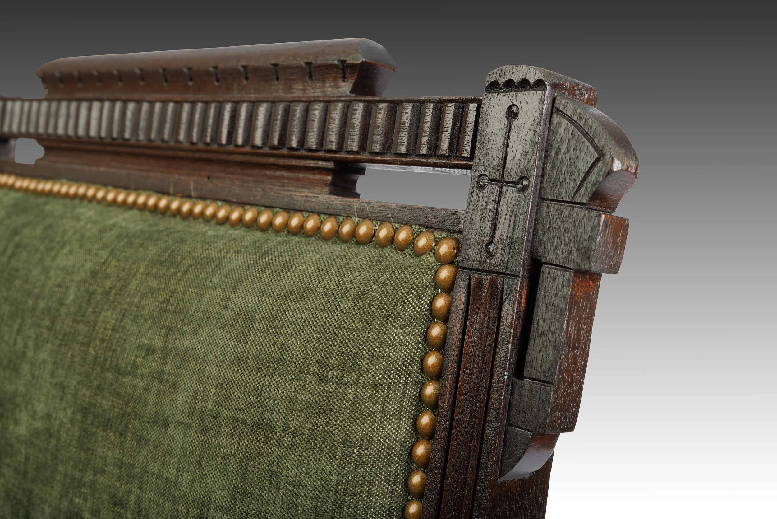 Detail of the restored Juniper Crest crest rail: a molded cap over a fluted, dentil-like band, a pierced gallery, and a block terminal incised with a fan, above green linen-blend upholstery with brass nailhead trim