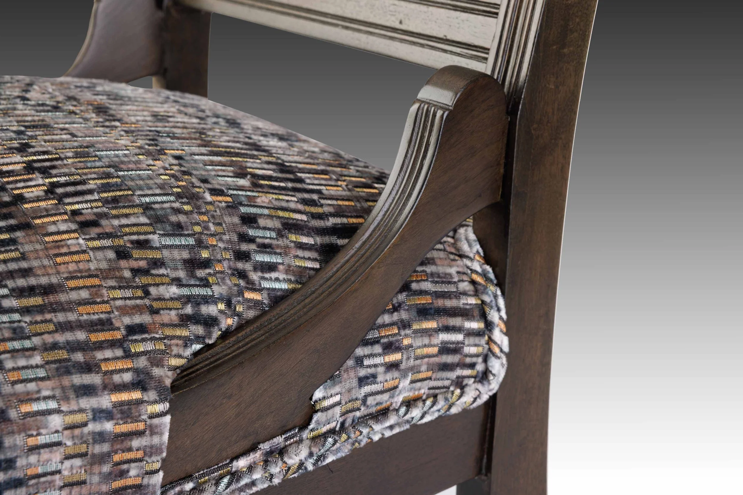 Detail of chair arm bracket and seat frame with pleated velvet and curved wood support.