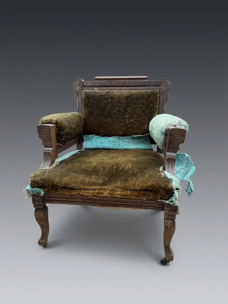 Pre-restoration front view of the Juniper Crest Eastlake armchair with worn olive-green velvet on the seat and back and torn turquoise fabric at the arm
