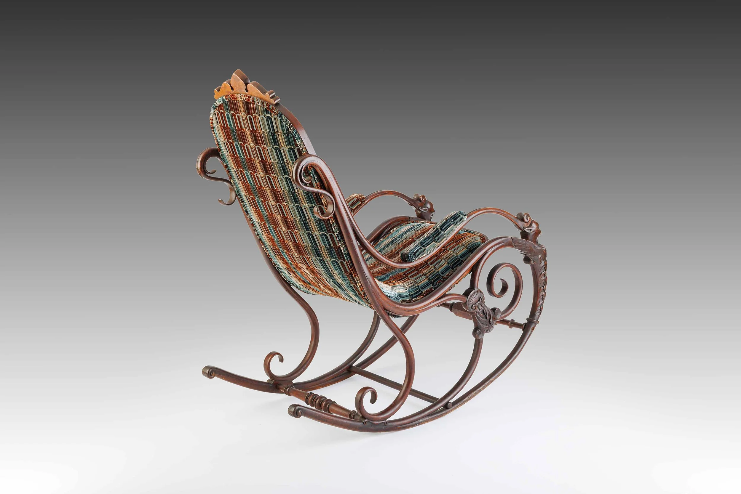 Rear angle of The Lioncourt Rocker, highlighting the flowing wood frame, scrollwork arms, and richly patterned textile.