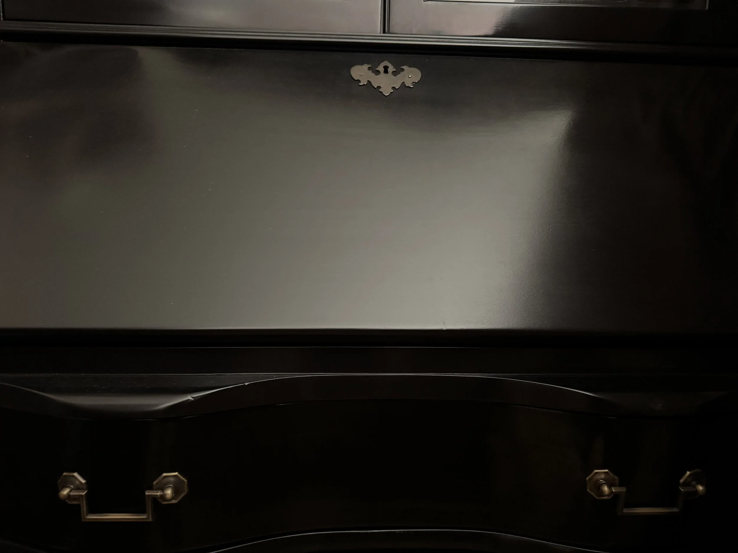 Closed fall-front writing surface with a pierced brass escutcheon, glazed doors above and a serpentine drawer with a rosette pull below, in black lacquer