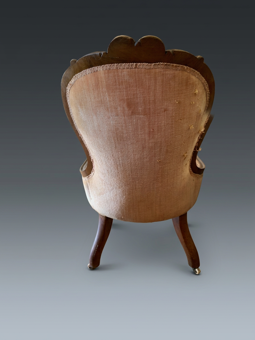 Reverse of the Victorian slipper chair before restoration, faded pink velvet with edge losses, carved frame and rear casters.