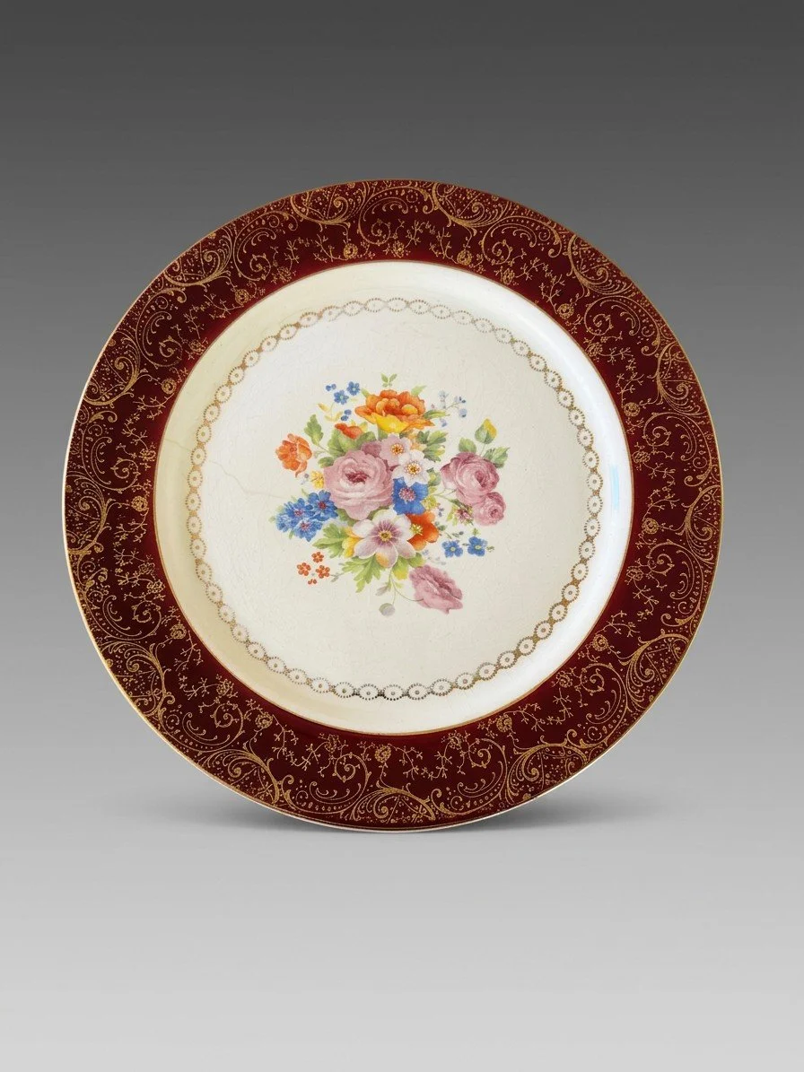 A maroon-rimmed plate with gilt scrollwork framing a floral bouquet on a finely crazed cream ground.