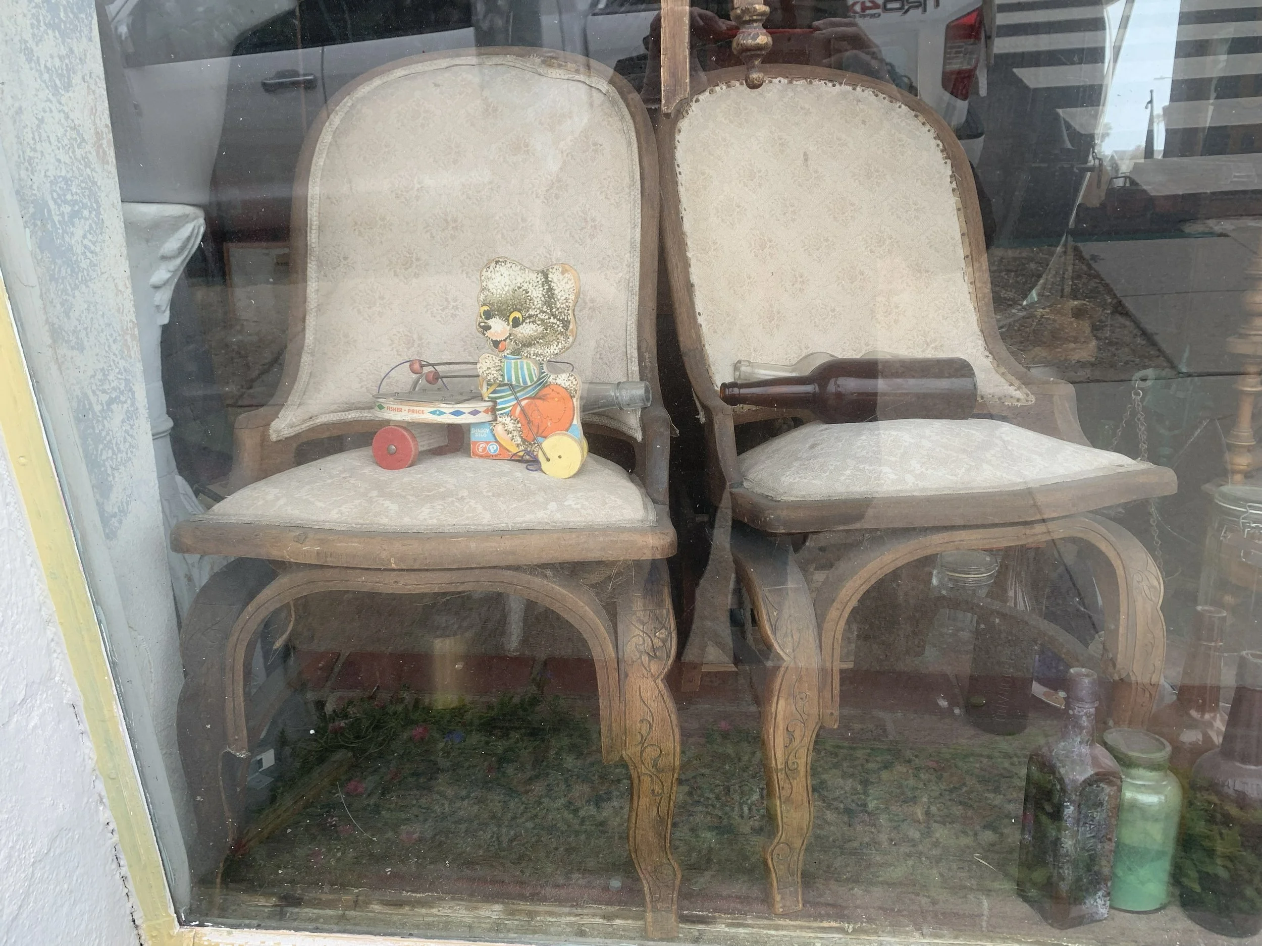 Antique Victorian reclining parlor chairs as found in a thrift shop window before restoration, in their earlier pale upholstery.