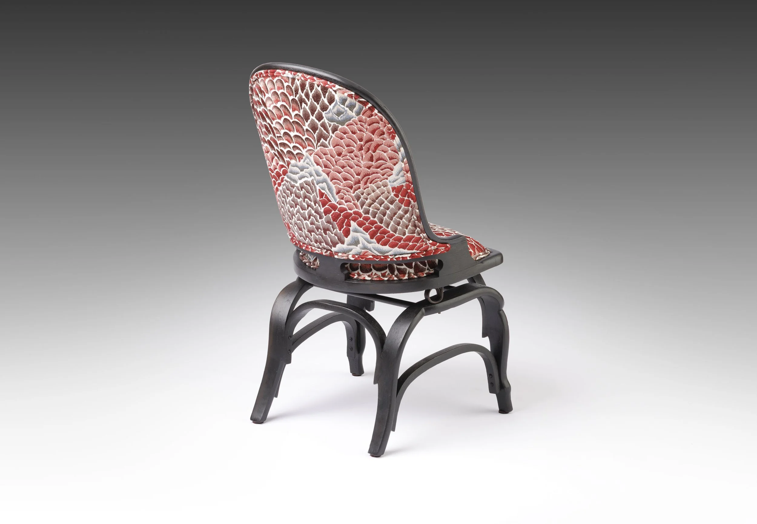 Ebonized parlor chair seen from the rear three-quarter, showing the curved spring-back frame and base