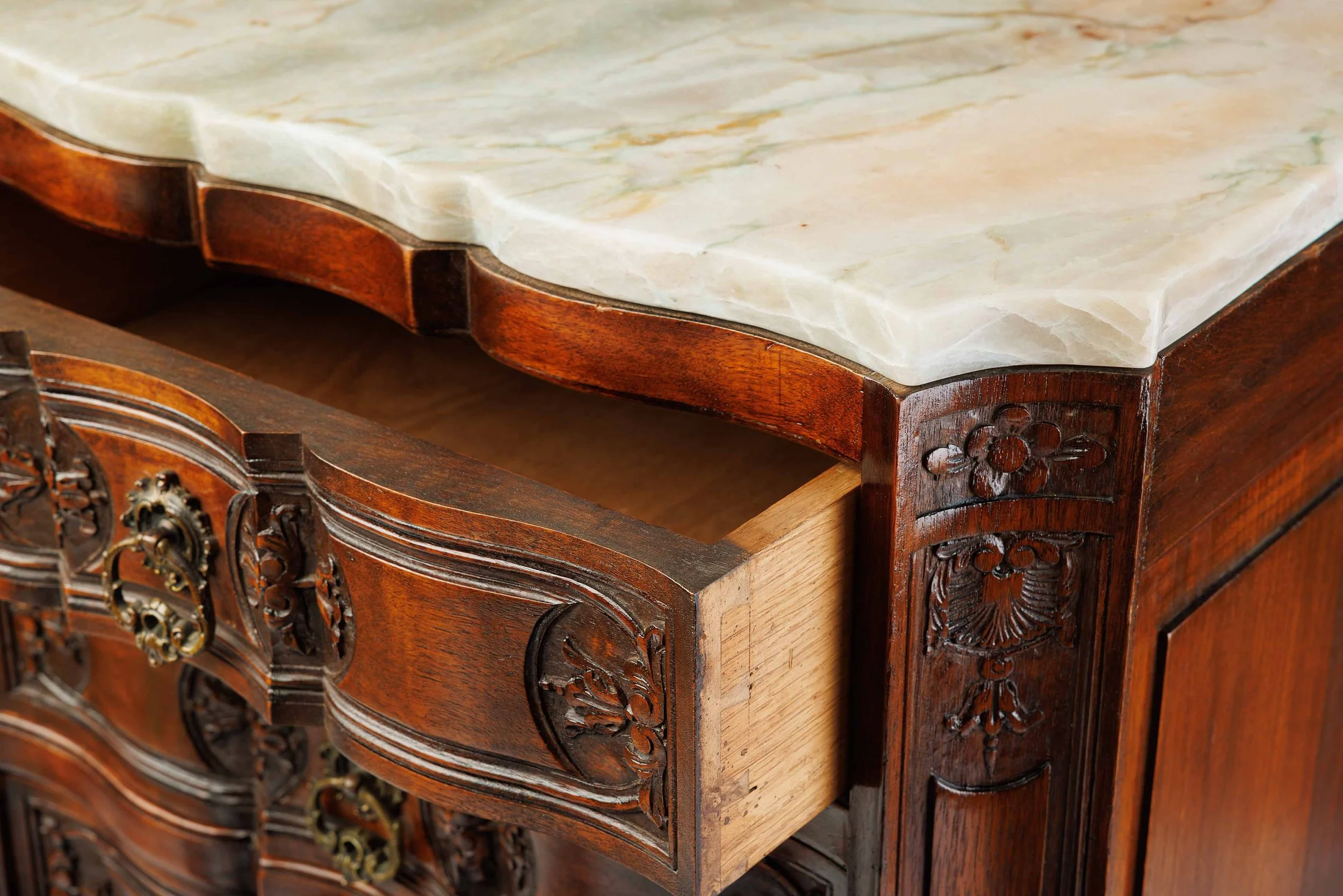 Angled detail of The Roseroot's quartzite top and upper carvings, including floral and shell motifs in rich-toned wood.