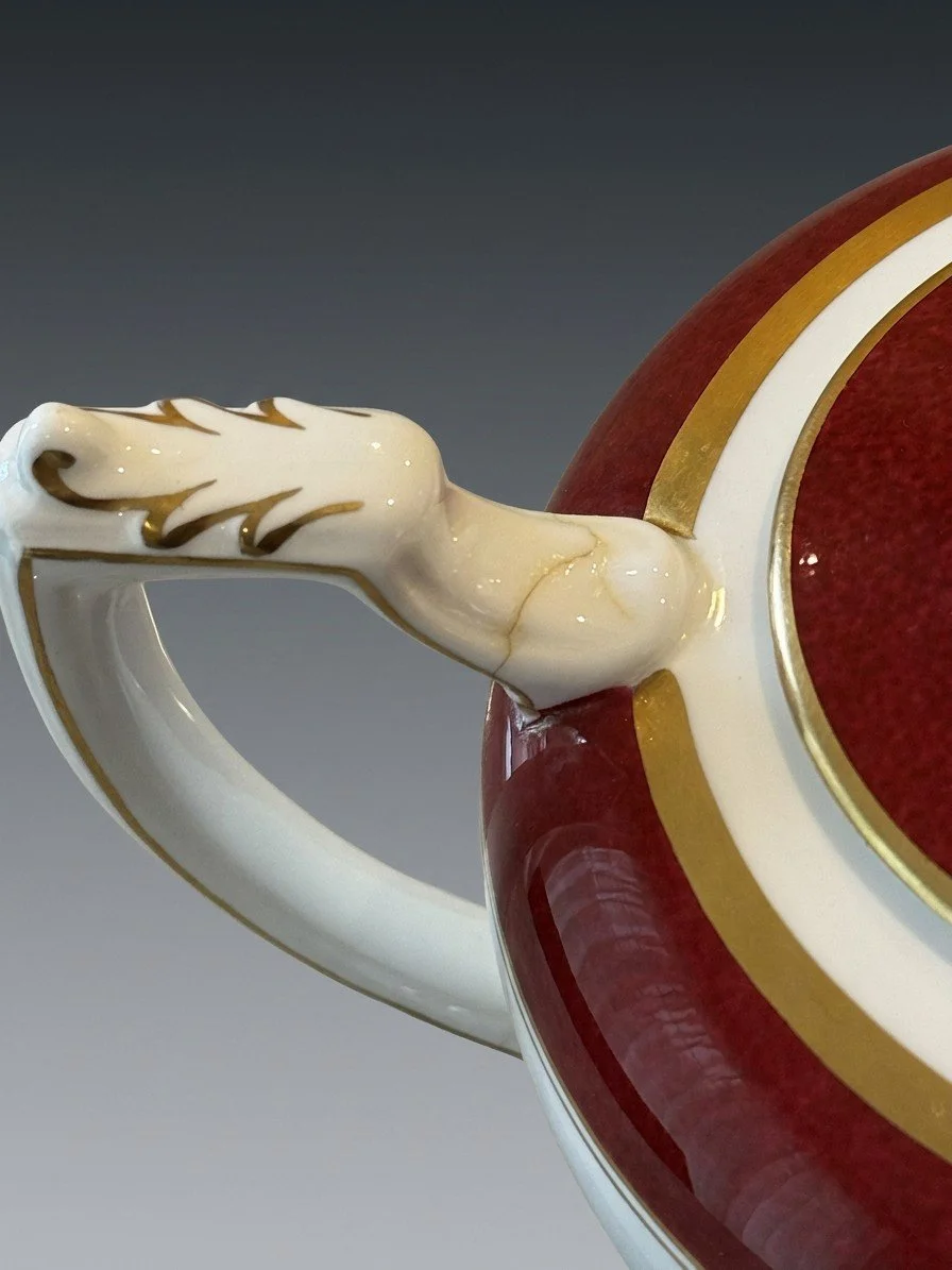 Detail of the teapot's gilt handle where it joins the body, a hairline stress crack darkened with use.