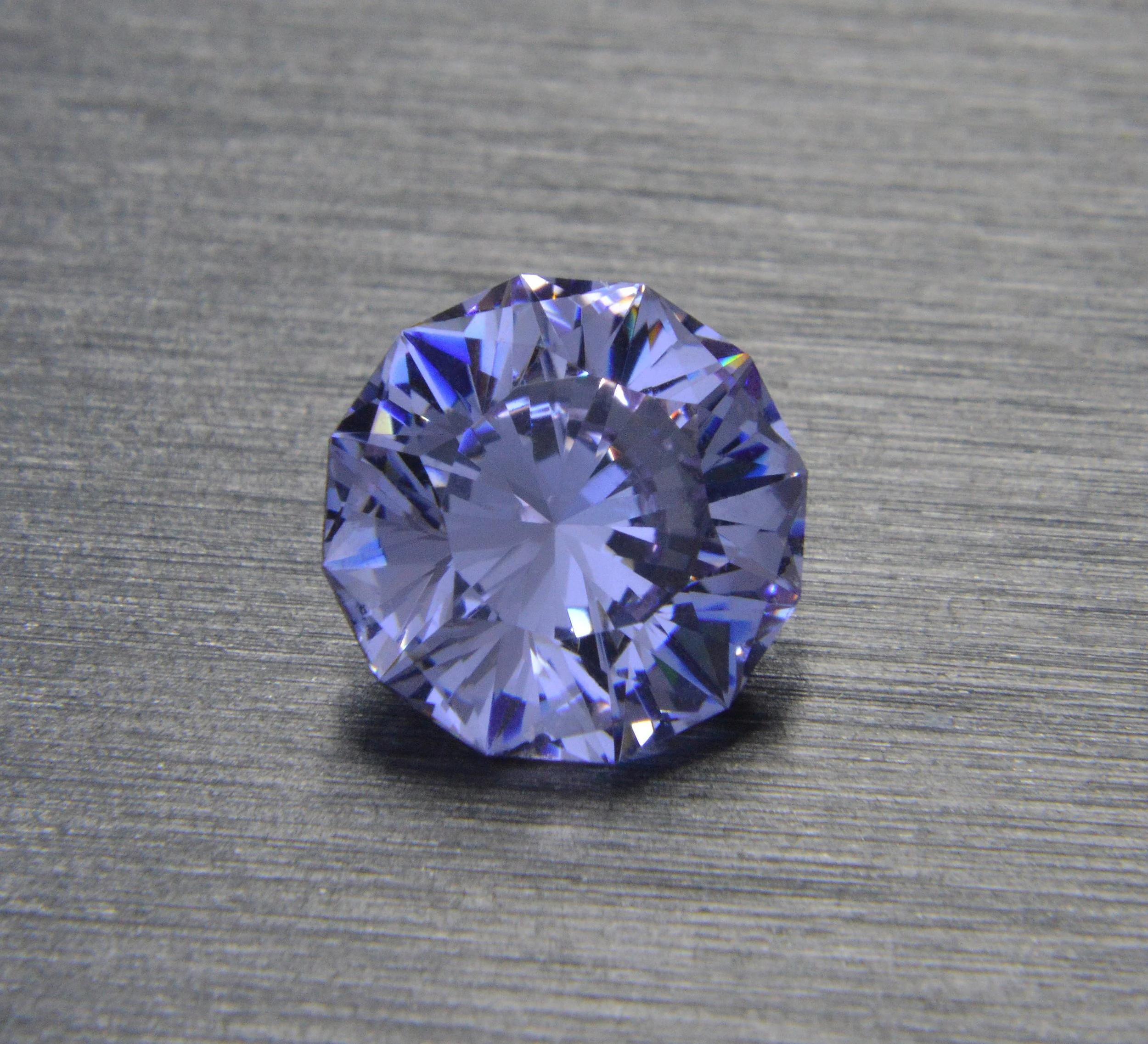 Close-up of a large, clear, faceted gemstone on a textured gray surface.