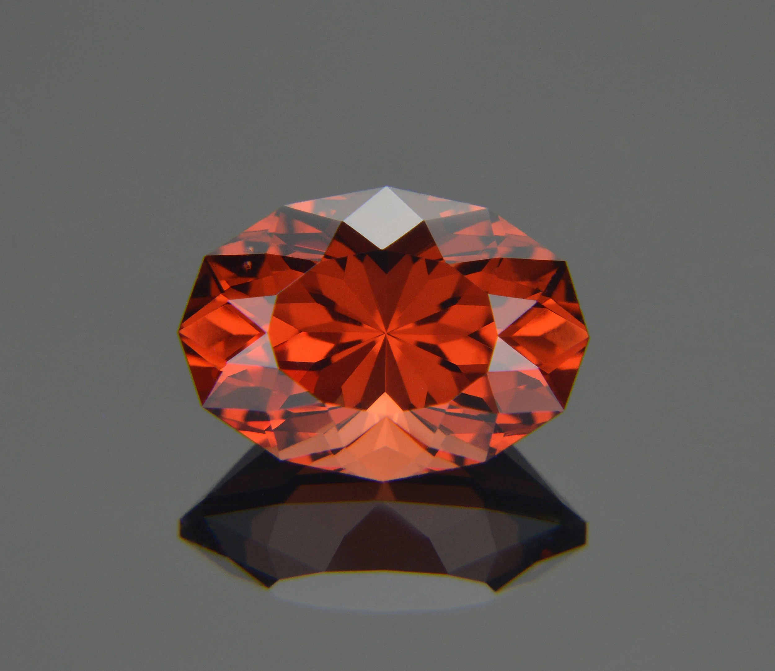 A round, faceted orange gemstone on a reflective surface with a gray background.