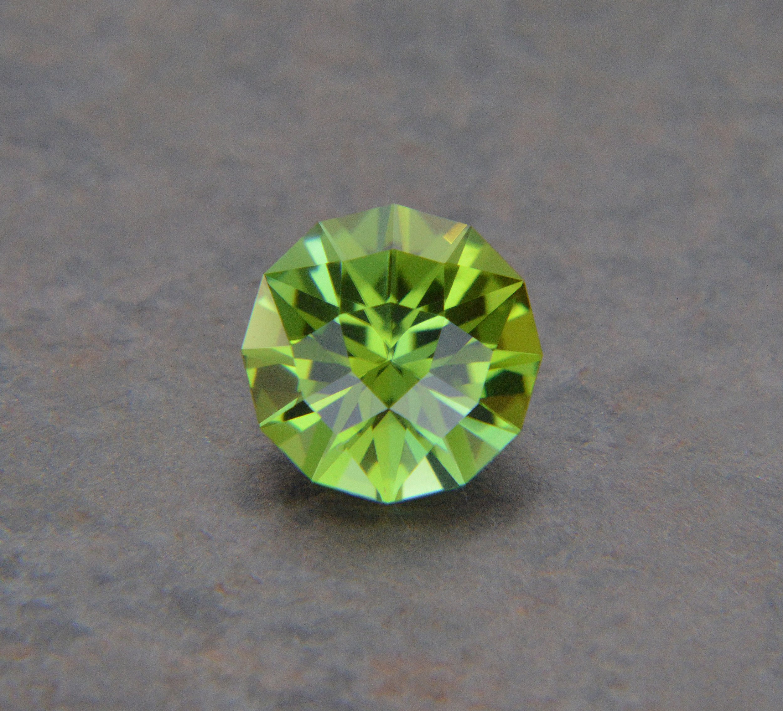 A green, faceted gemstone on a gray surface.