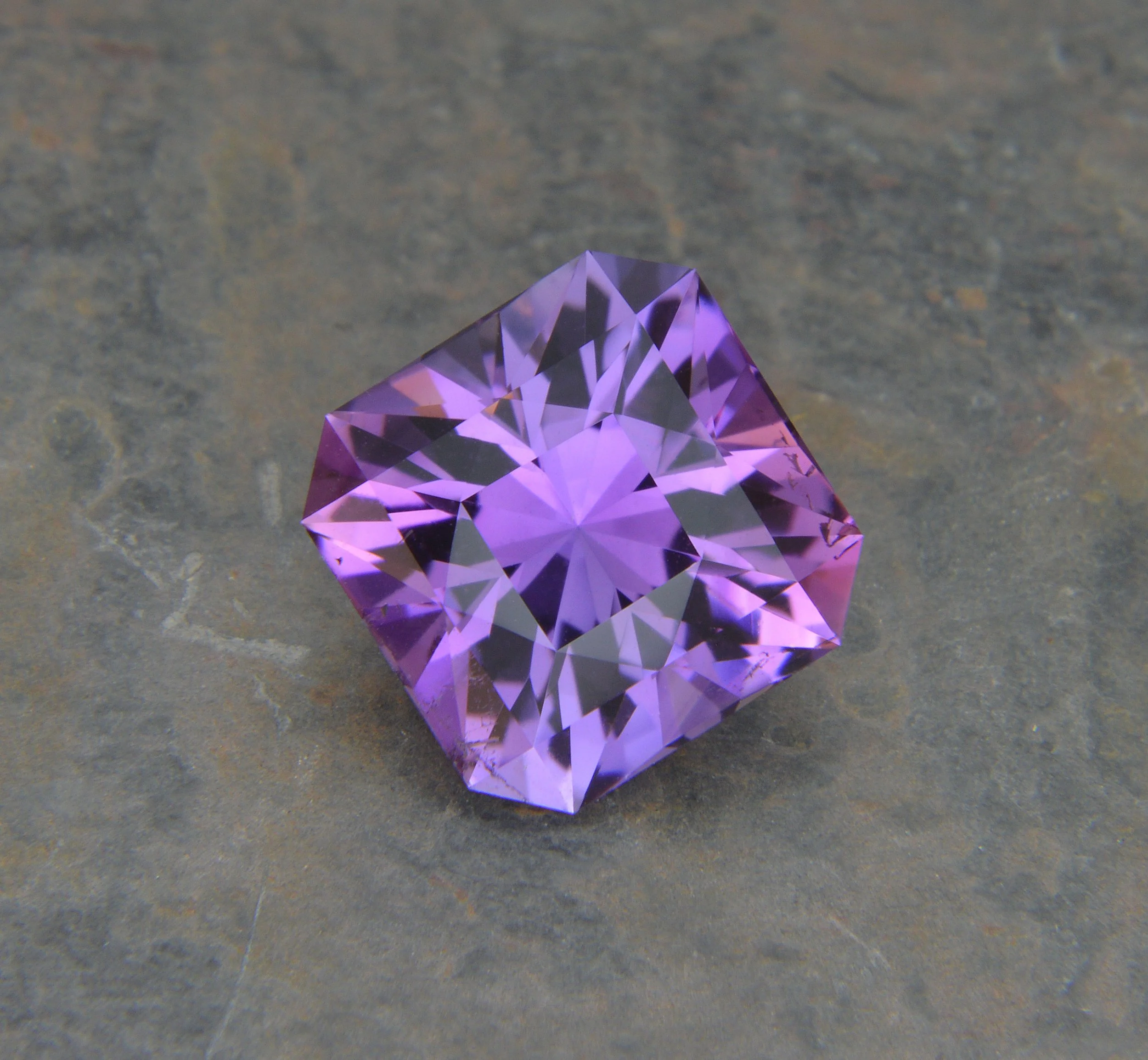 A purple, faceted gemstone cube on a stone surface.