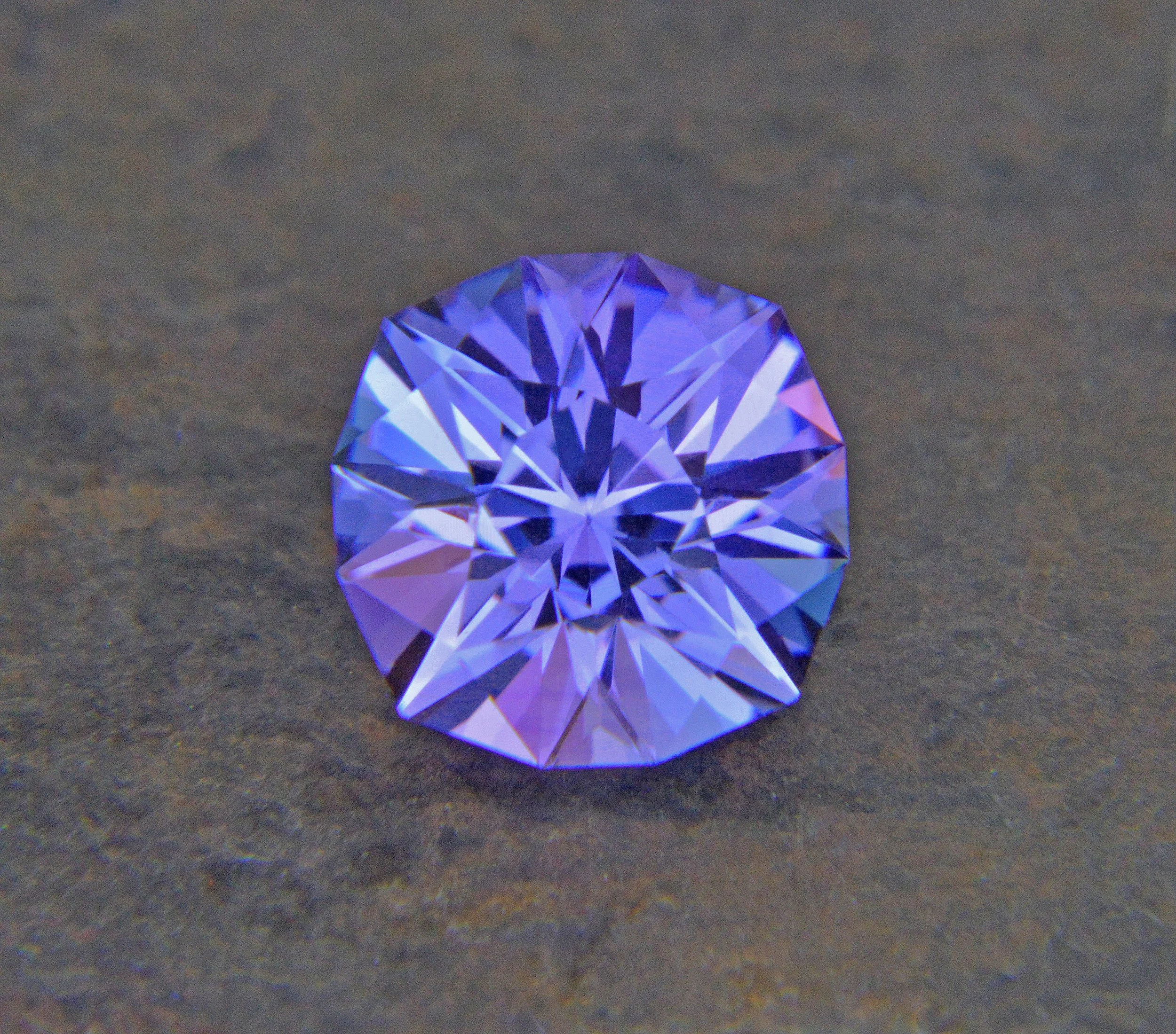 A close-up photo of a sparkling, faceted purple gemstone on a textured surface.