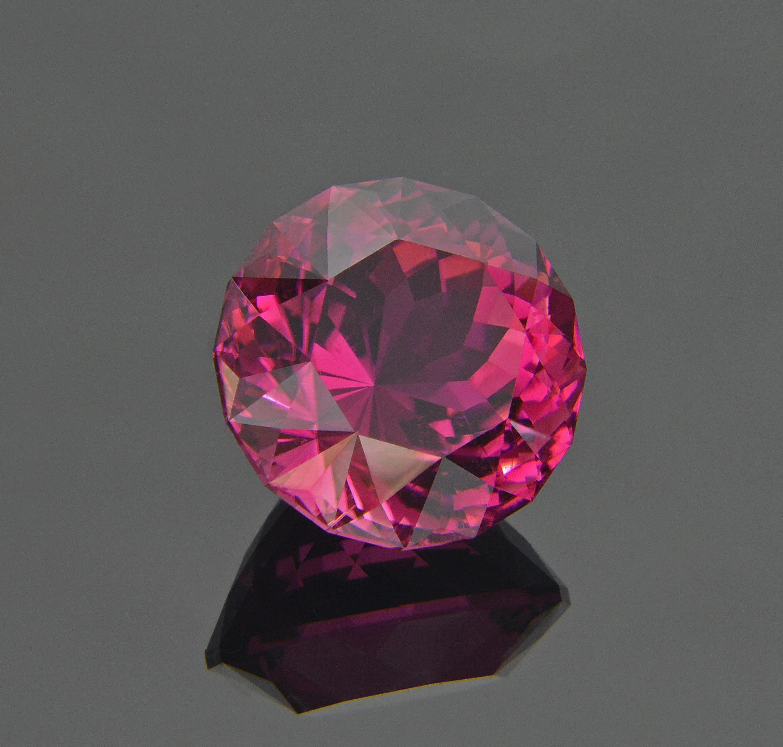 A pink gemstone with multiple facets, reflecting light, placed on a black reflective surface.