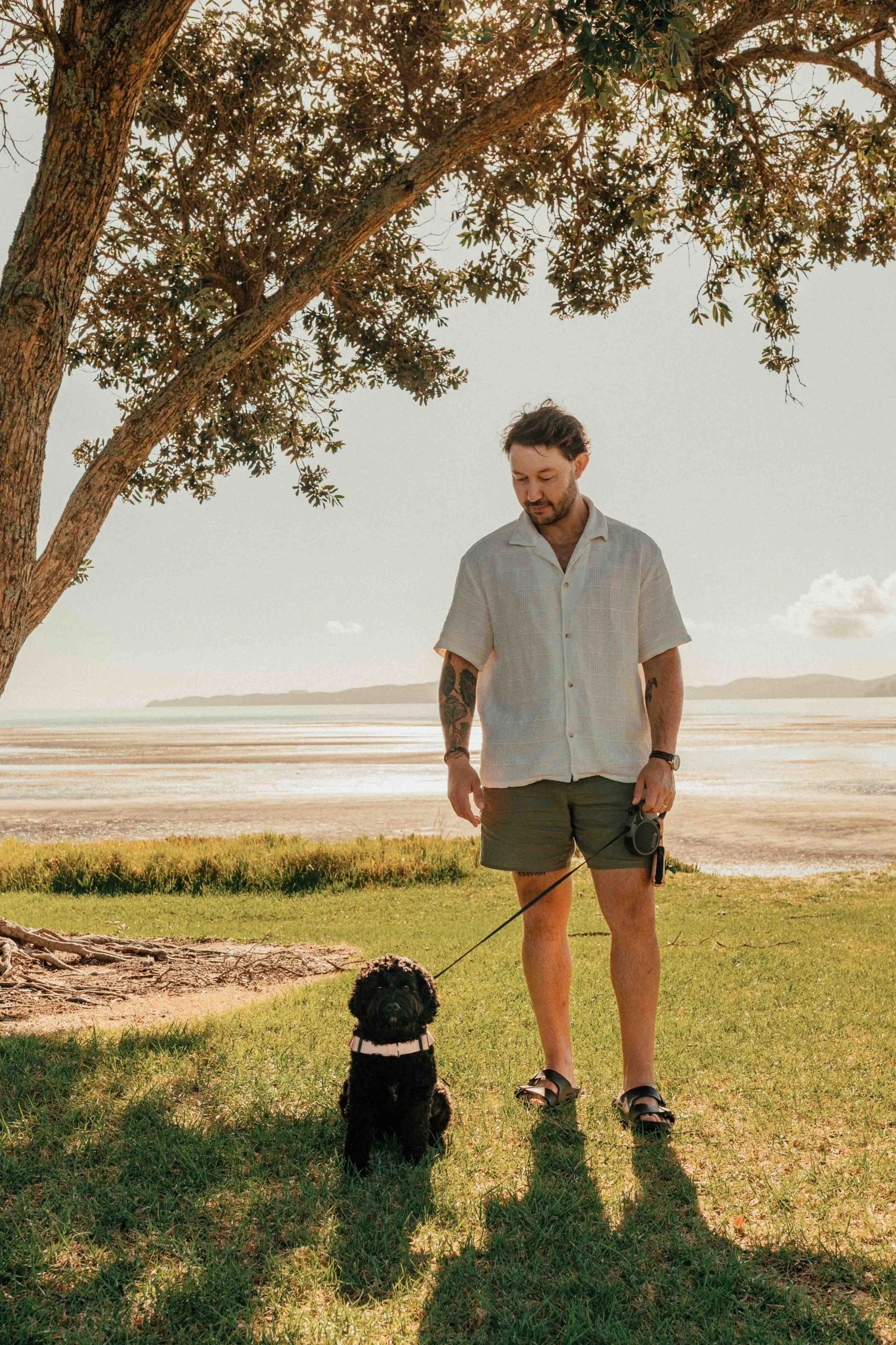 Man stands on beach with black dog. Sea and island behind them in the distance.