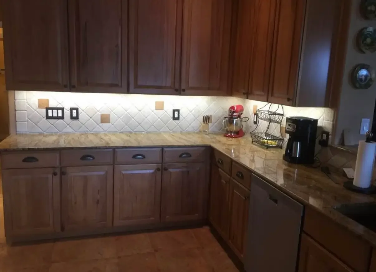 Warm, well-lit residential kitchen featuring under-cabinet LED lighting that enhances granite countertops and tiled backsplash. This installation highlights energy-efficient kitchen lighting, improved task illumination, and professional electrical up
