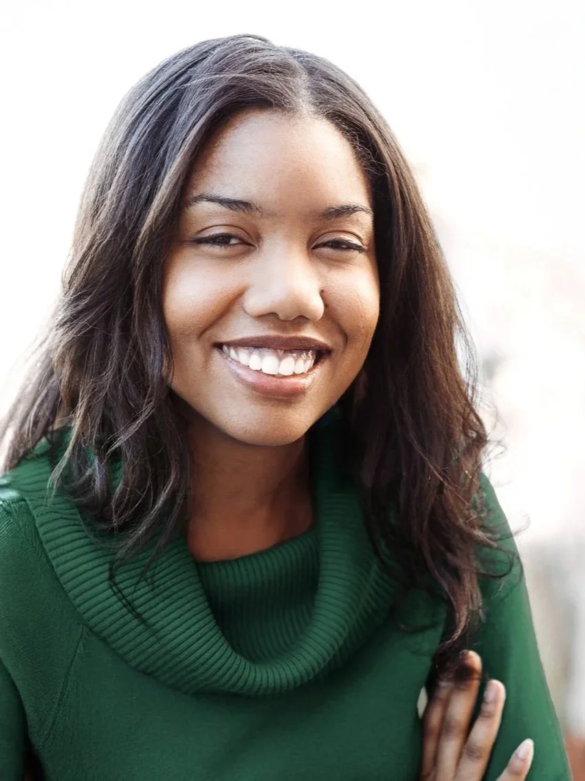 A smiling woman with long dark hair, wearing a green sweater, posing outdoors.