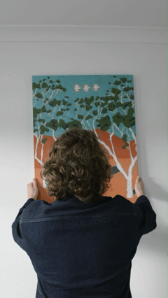 Person with curly hair wearing a dark jacket looking at a colorful abstract painting on the wall.