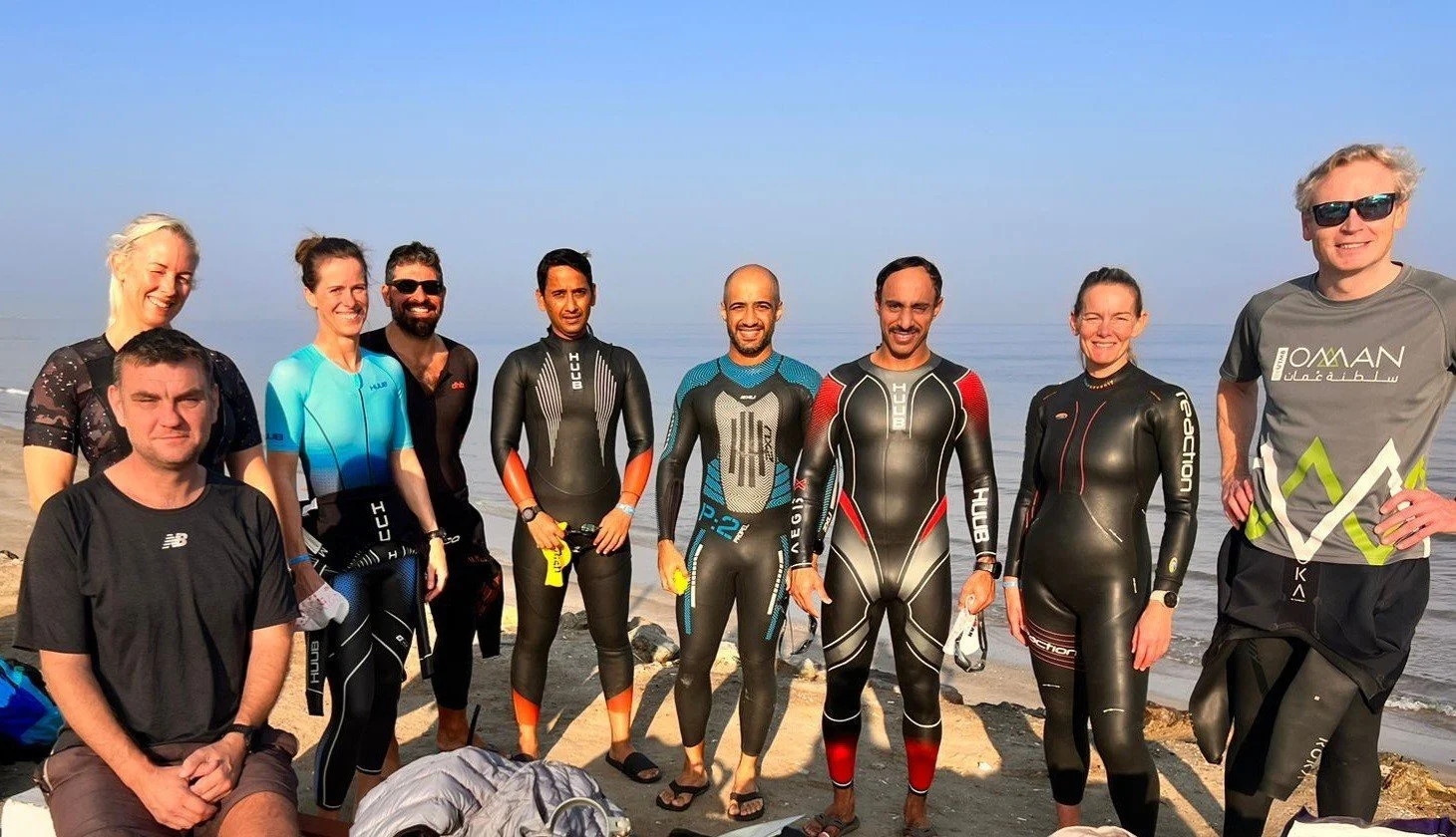 Group of people in wetsuits standing on a beach with the ocean in the background during daytime.