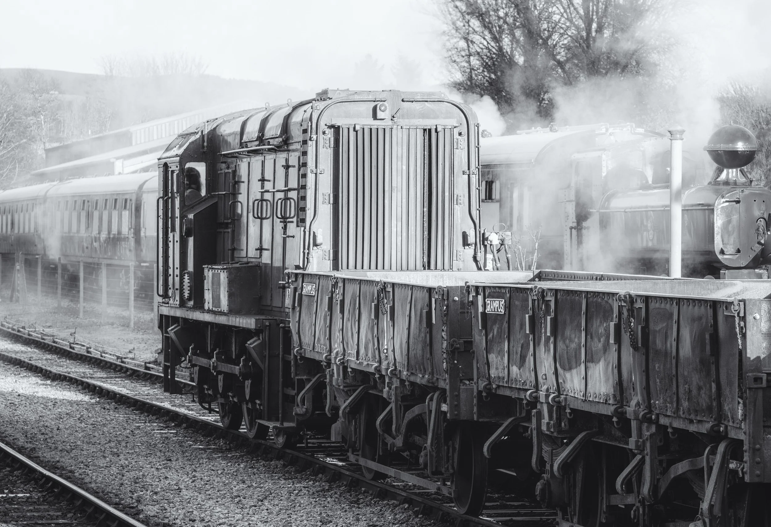 Black and white photograph of an old steam train on the tracks with smoke coming out of the engine and a train car attached.