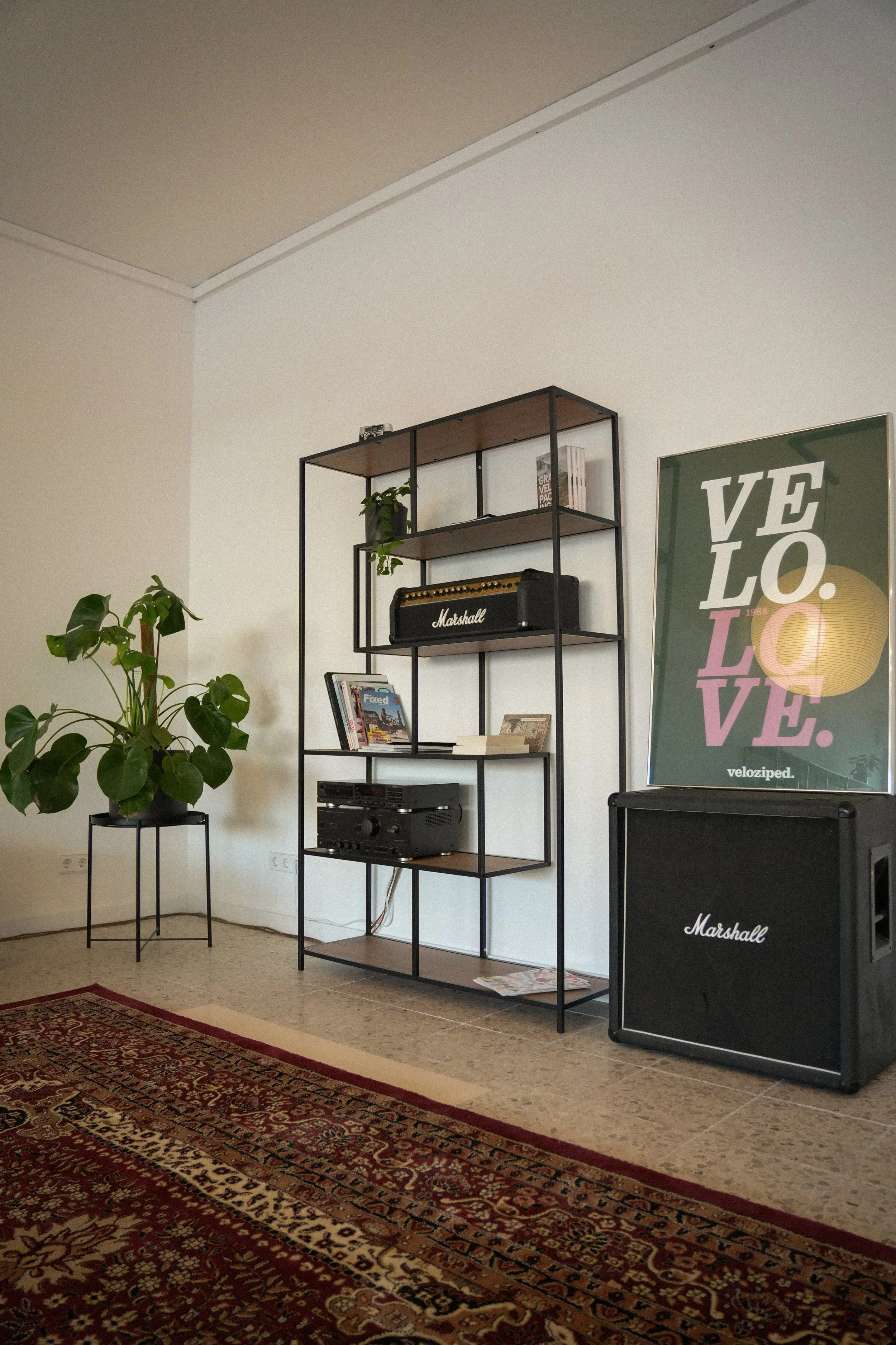 Wohnzimmer mit schwarzem Metallregal, Marshall Verstärker, Plattenspieler, Pflanzen und einem großen Kunstposter mit "VELOLOVE" Schriftzug