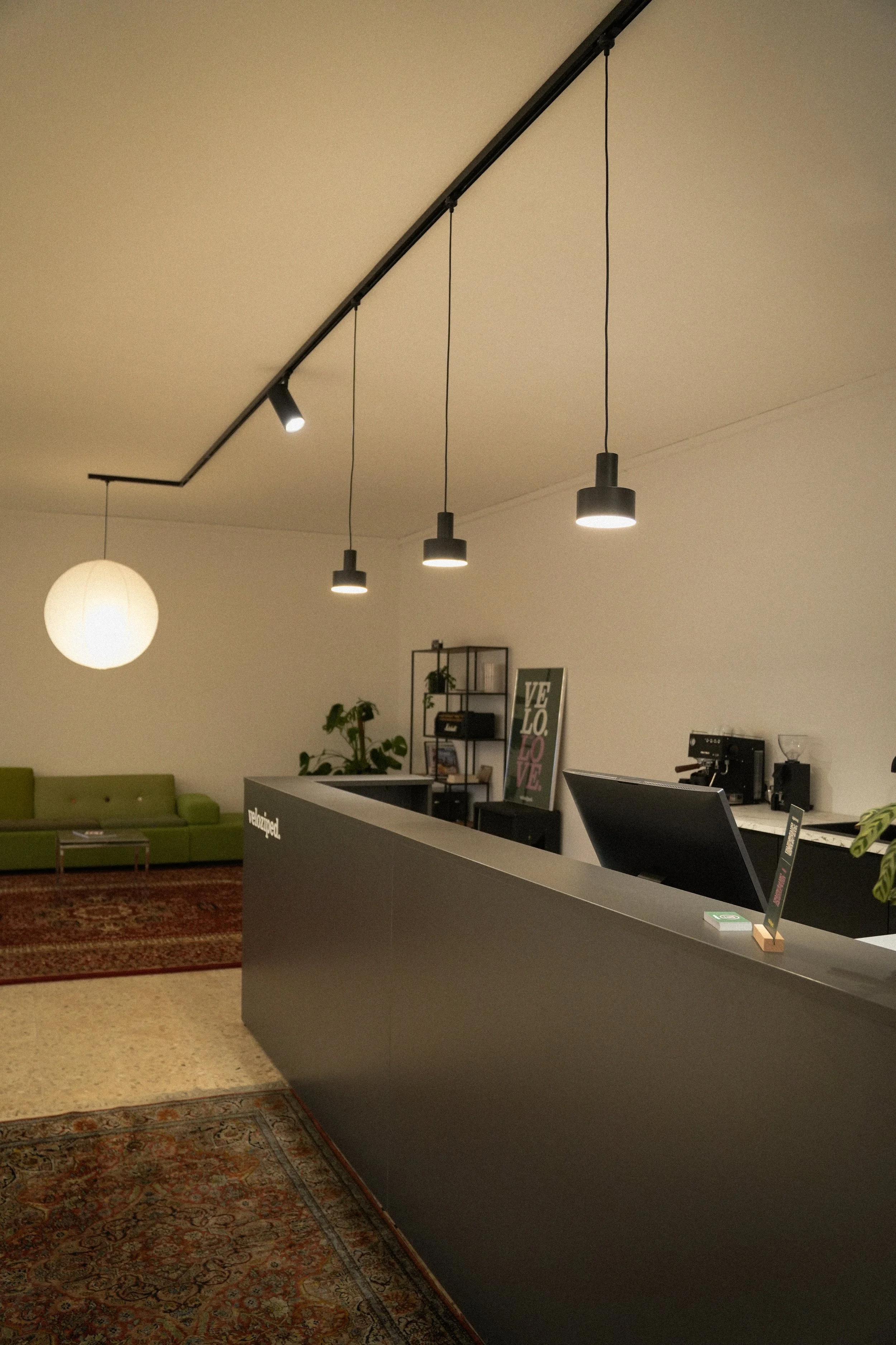 Ein Empfangstresen in einem modernen Raum mit einer schwarzen Oberfläche, umgeben von einem grünen Sofa und einem Bücherregal im Hintergrund, Beleuchtung von Deckenleuchten.