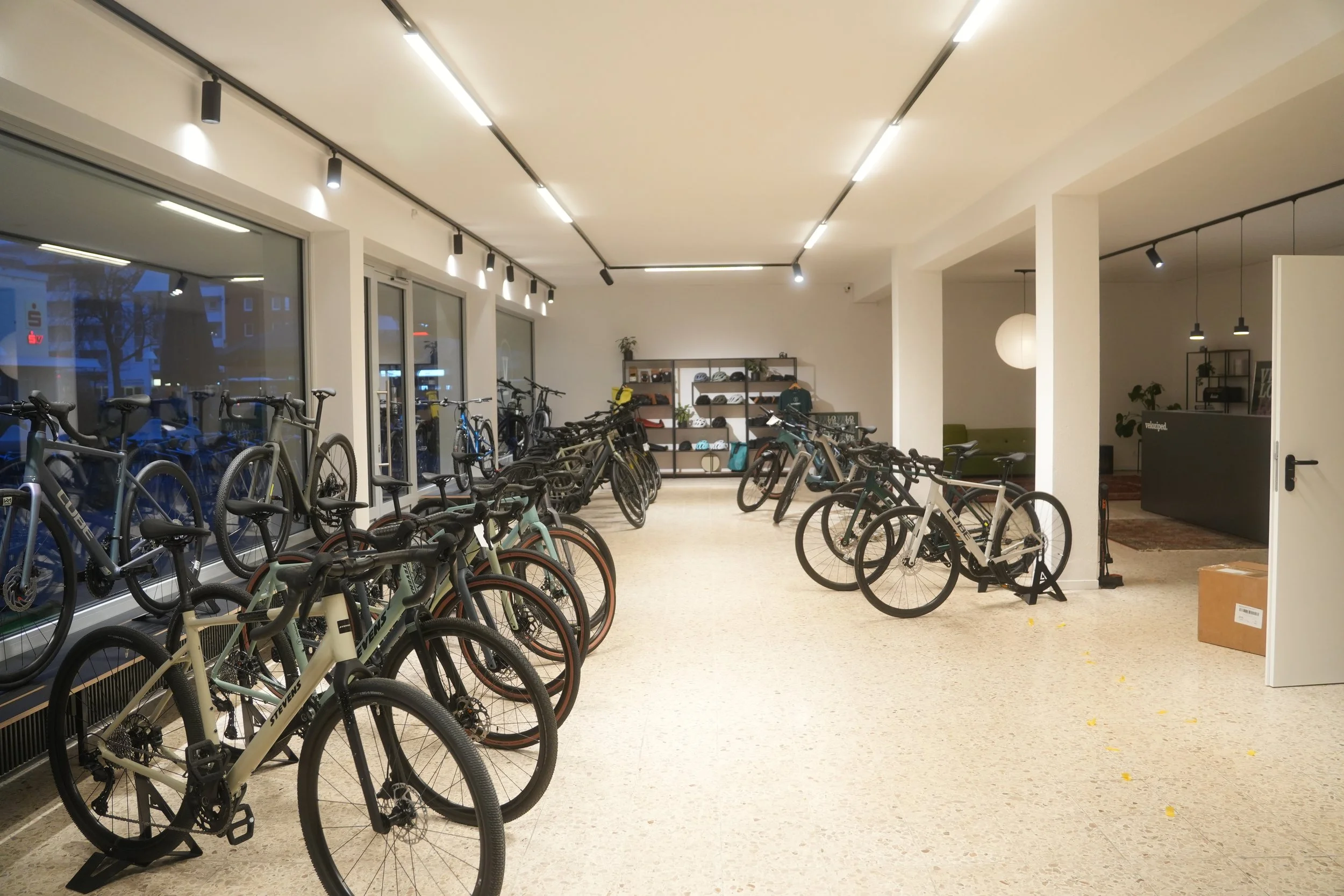 Innenraum eines Fahrradkellers mit mehreren abgestellten Fahrrädern und einer Wand mit Regalen, die Helme und andere Gegenstände halten.