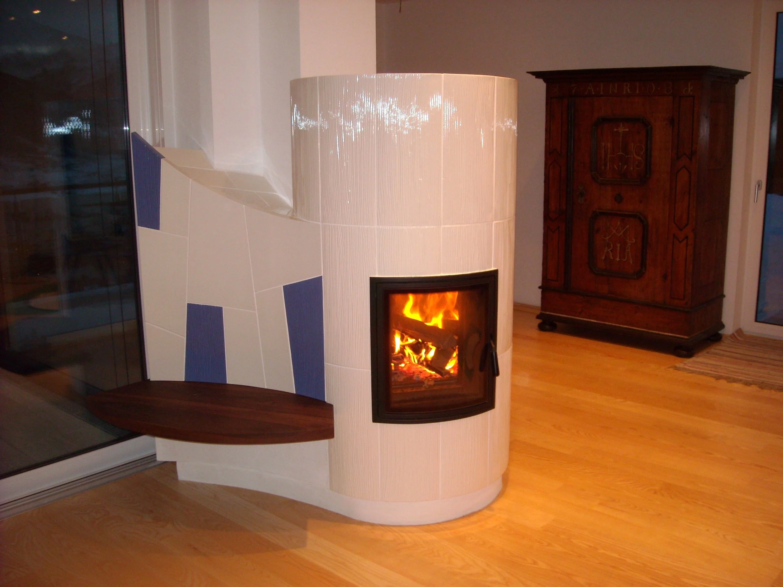 Ein moderner, runder Kamin mit Flammen, umgeben von weißen Fliesen mit blauen Akzenten.