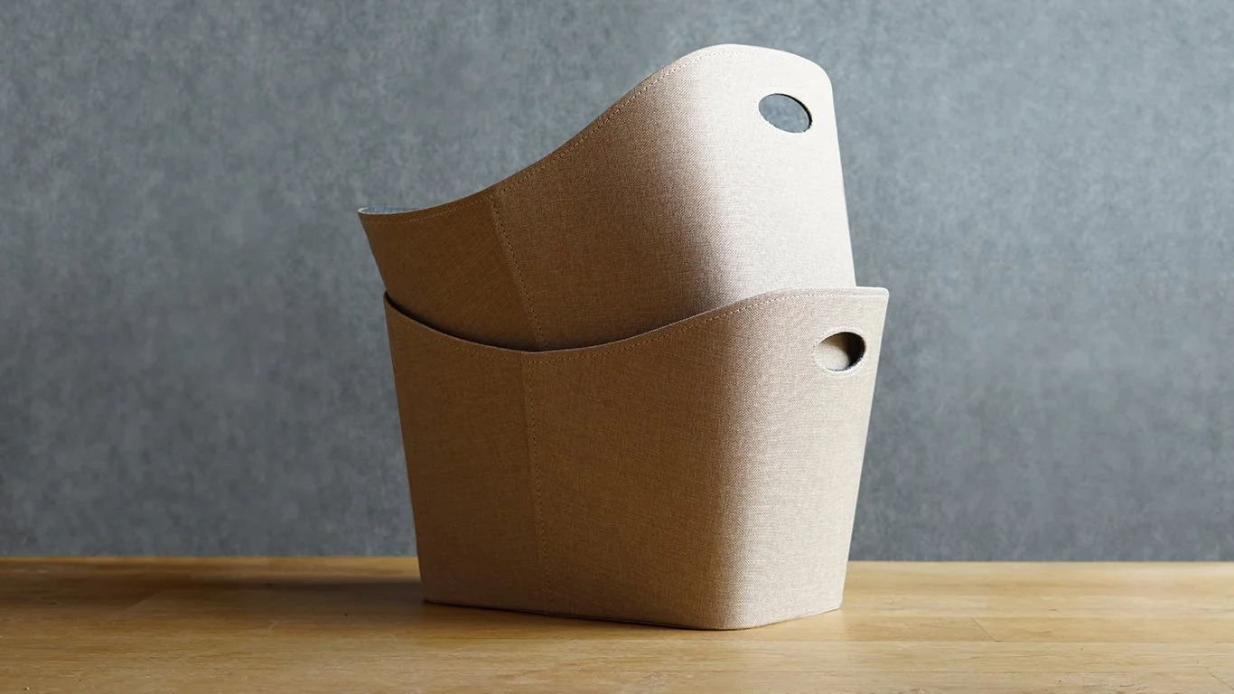 Zwei beige Stoffkorb auf einem Holztablett vor grauer Wand.