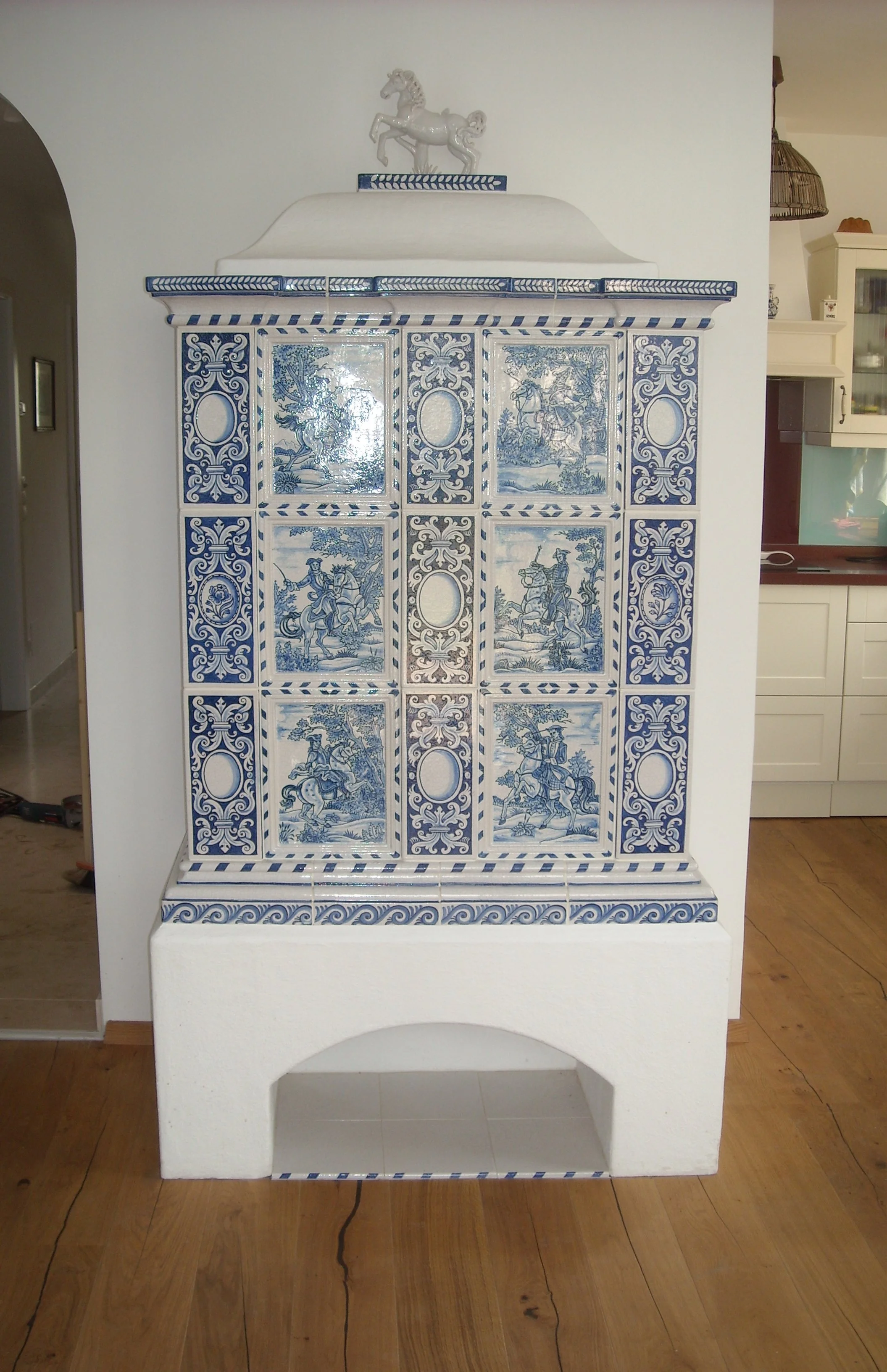 EIn blau-weißer Kachelofen mit Engravings und einer weißen Statue eines Pferdes auf der Oberseite.