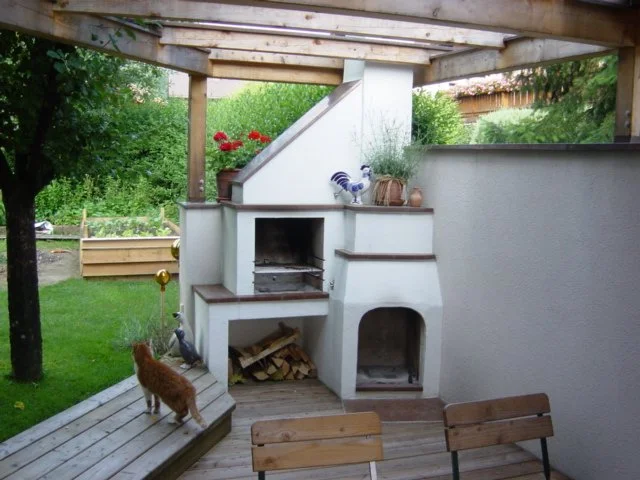 Garten mit offenem Kamin und Holzofen, im Hintergrund Bepflanzung und Gartenbeet.