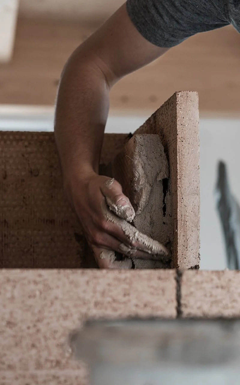 Hand eines Maurers beim Legen eines Ziegelsteins auf eine Mauer