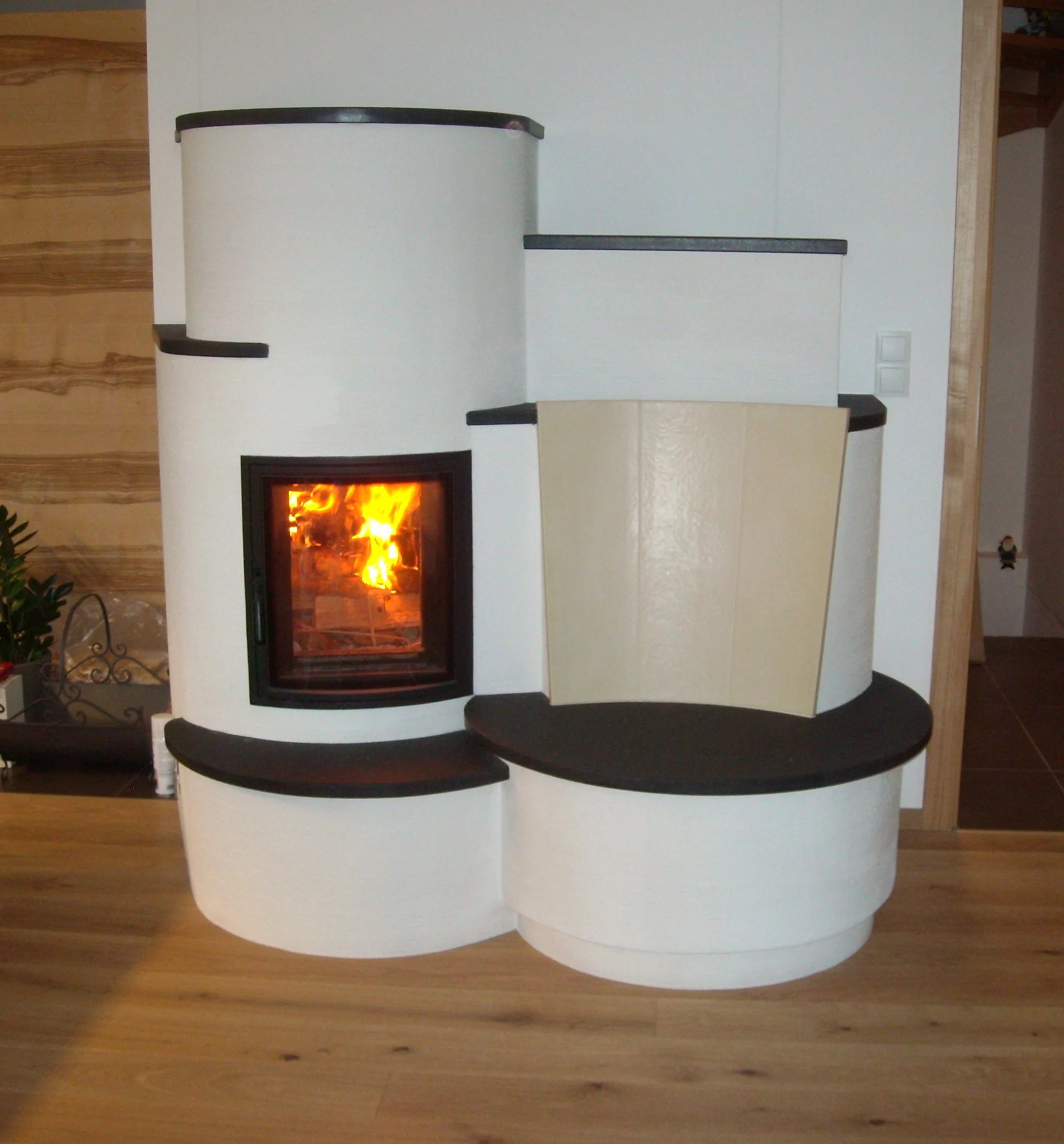 Moderner Kamin mit dunklen Details und sichtbarem Feuer vor weißer Wand.