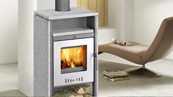 Ein Kamin mit Feuer, daneben ein moderner Lese-Sessel und einige Zeitschriften.