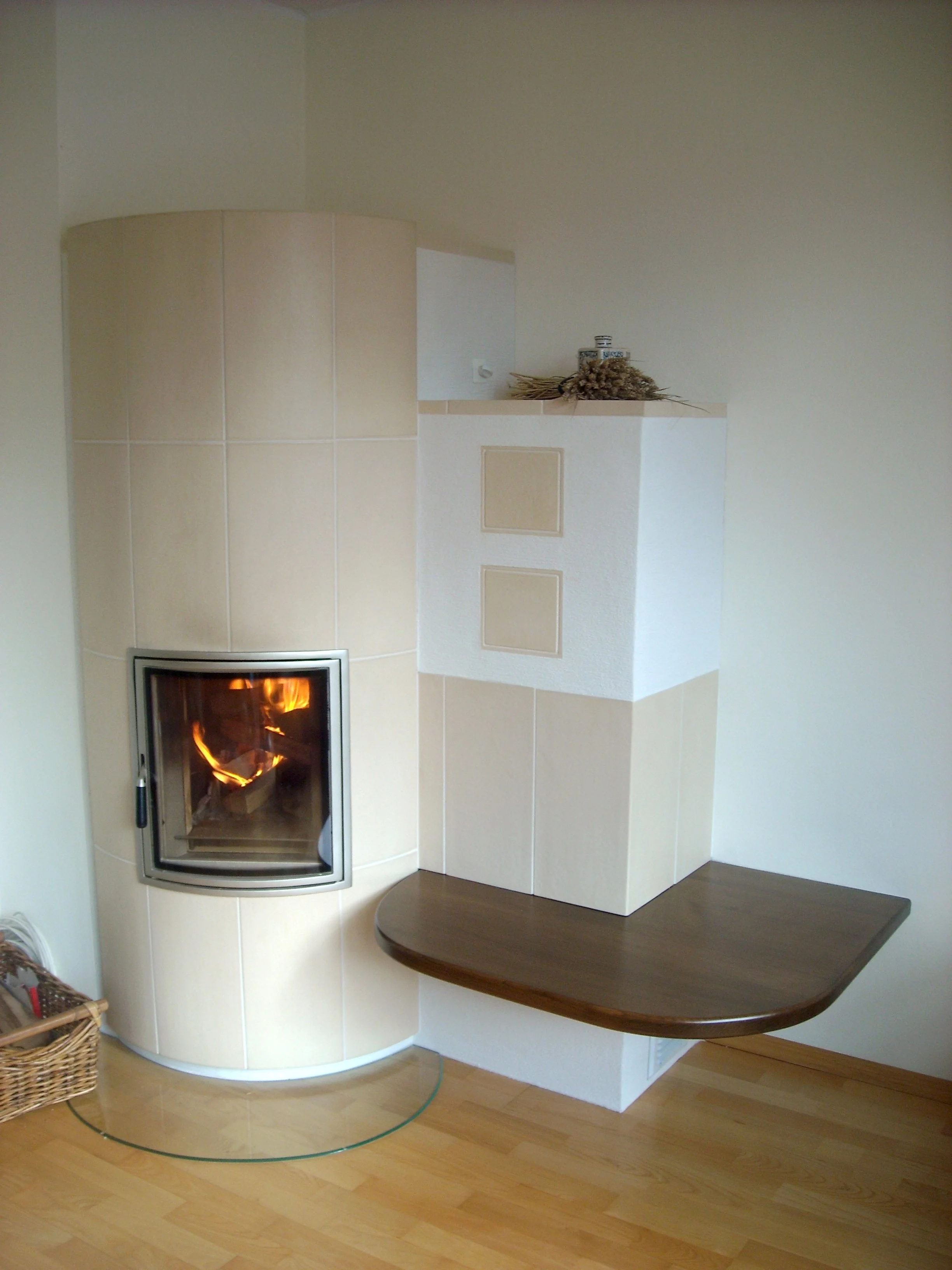 Ein Kamin im Wohnzimmer, umgeben von beigen Fliesen, eine Holzbank an der Seite und Dekorationen obenauf.