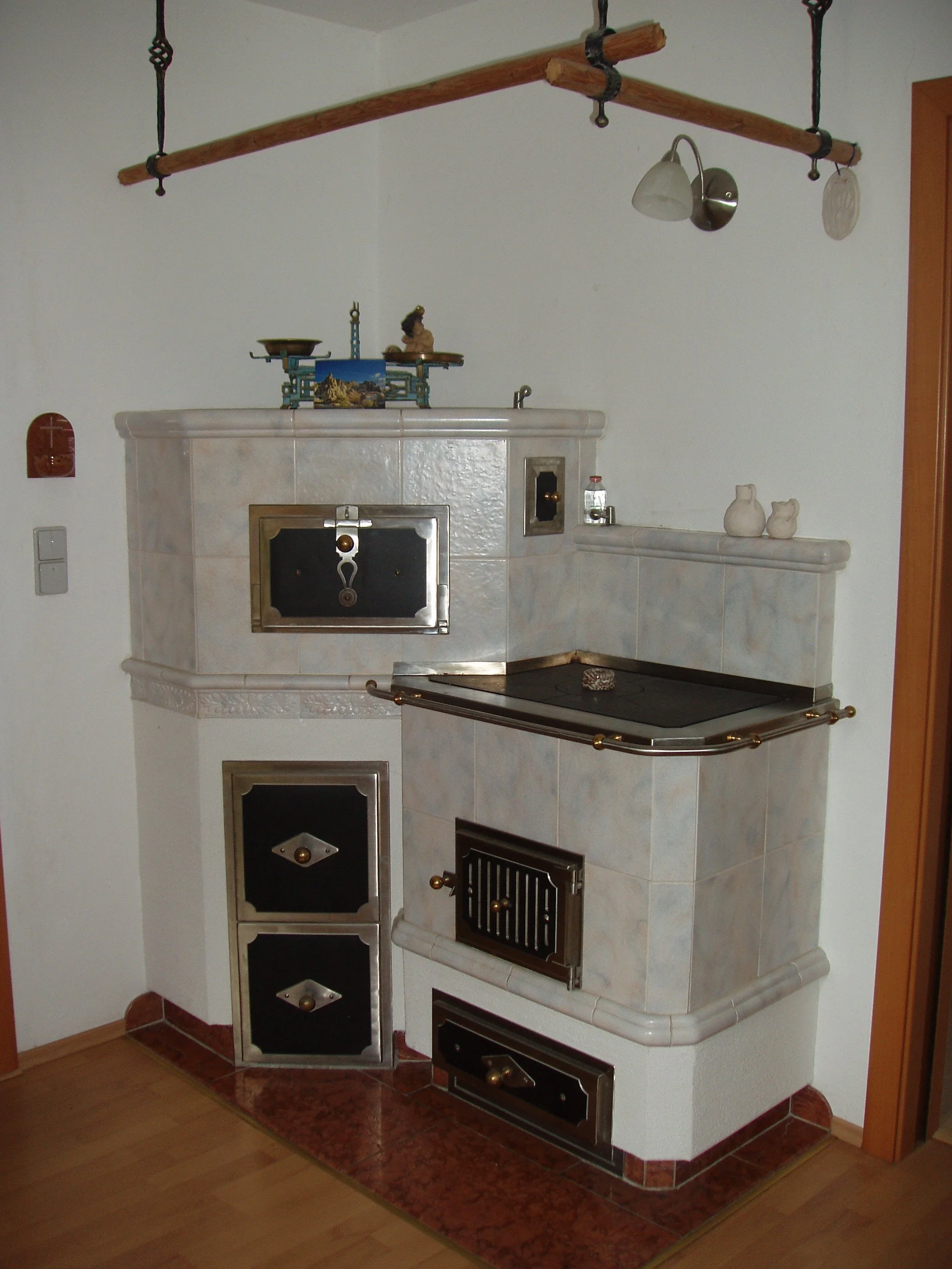 Traditioneller Keramikofen in einer Holz-Küche, mit kleinen Dekorationsgegenständen auf der Oberseite.