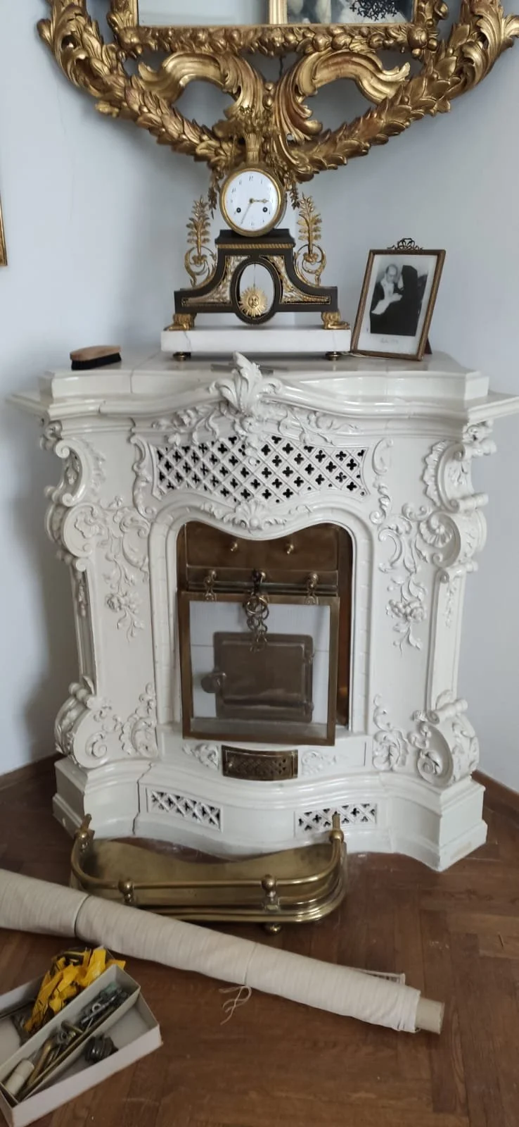 Ein eleganter, weißer, kunstvoll verzierter Kaminofen mit einem goldenen, alten Spiegel darüber.