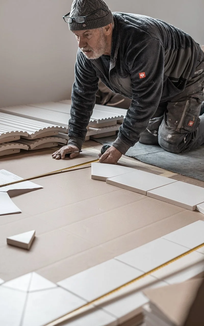 Ein älterer Mann legt Fliesen in einem Innenraum.