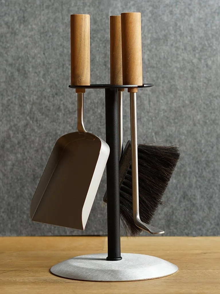 Hochwertiger Teelichthalter mit Holzgriffen und Reinigungsutensilien wie Staubwedel, Besen, und Schaufel, auf Holztisch vor grauem Hintergrund.