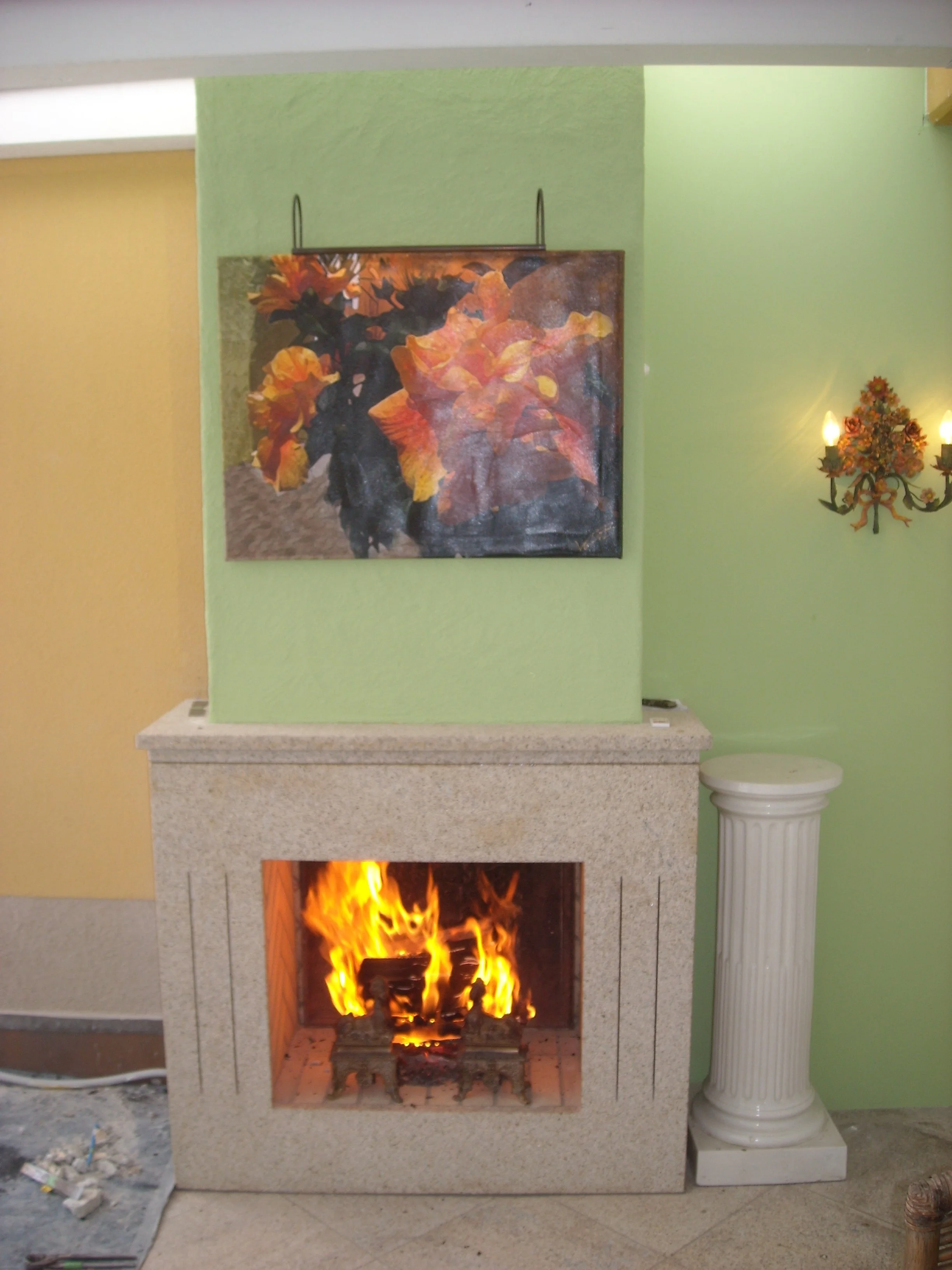 Kamin mit brennendem Feuer, darüber ein Gemälde mit bunten Blumen, an der Seite eine dekorative Wandleuchte und eine Säule