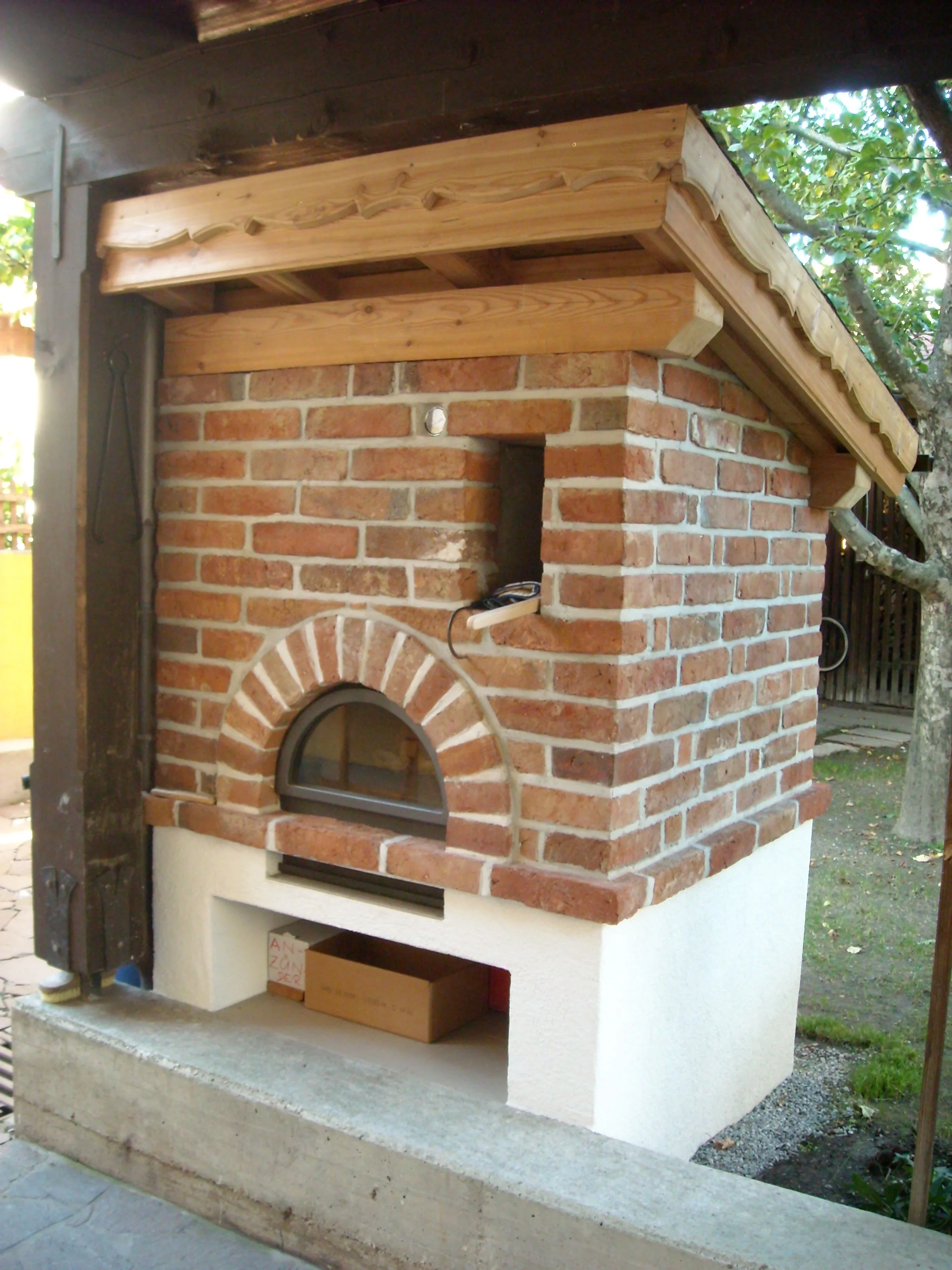 Ein gemauerter Pizzaofen mit einem halbkreisförmigen Fenster und einer Holzabdeckung.