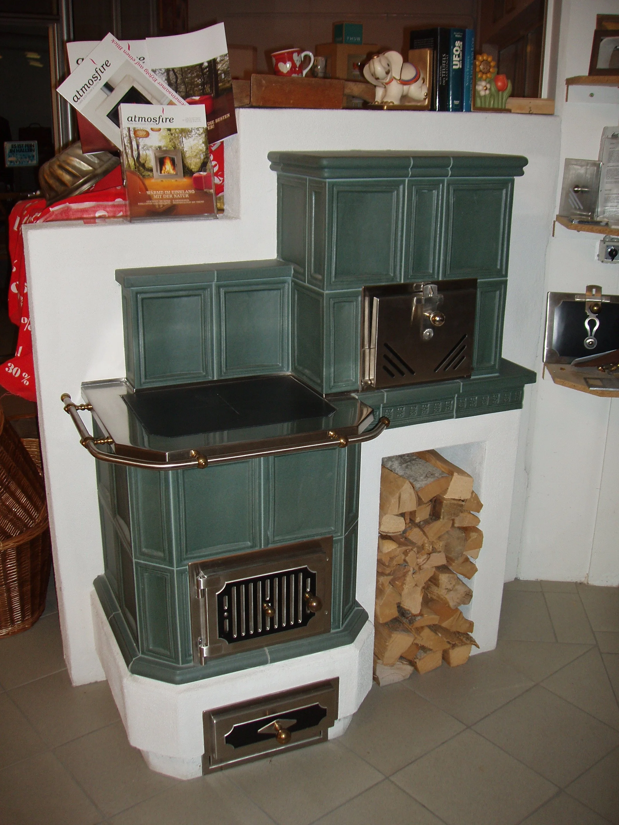 Ein traditioneller Kachelofen mit Holzfach und Backofen, verziert mit Bronzegriffen, in einem Raum mit Büchern und Dekorationen.