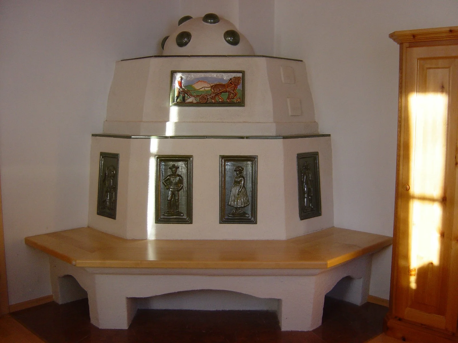 Ein traditioneller Kachelofen mit schönen grünen Kacheln, in einem Raum mit weißer Wand und Holzmöbeln.