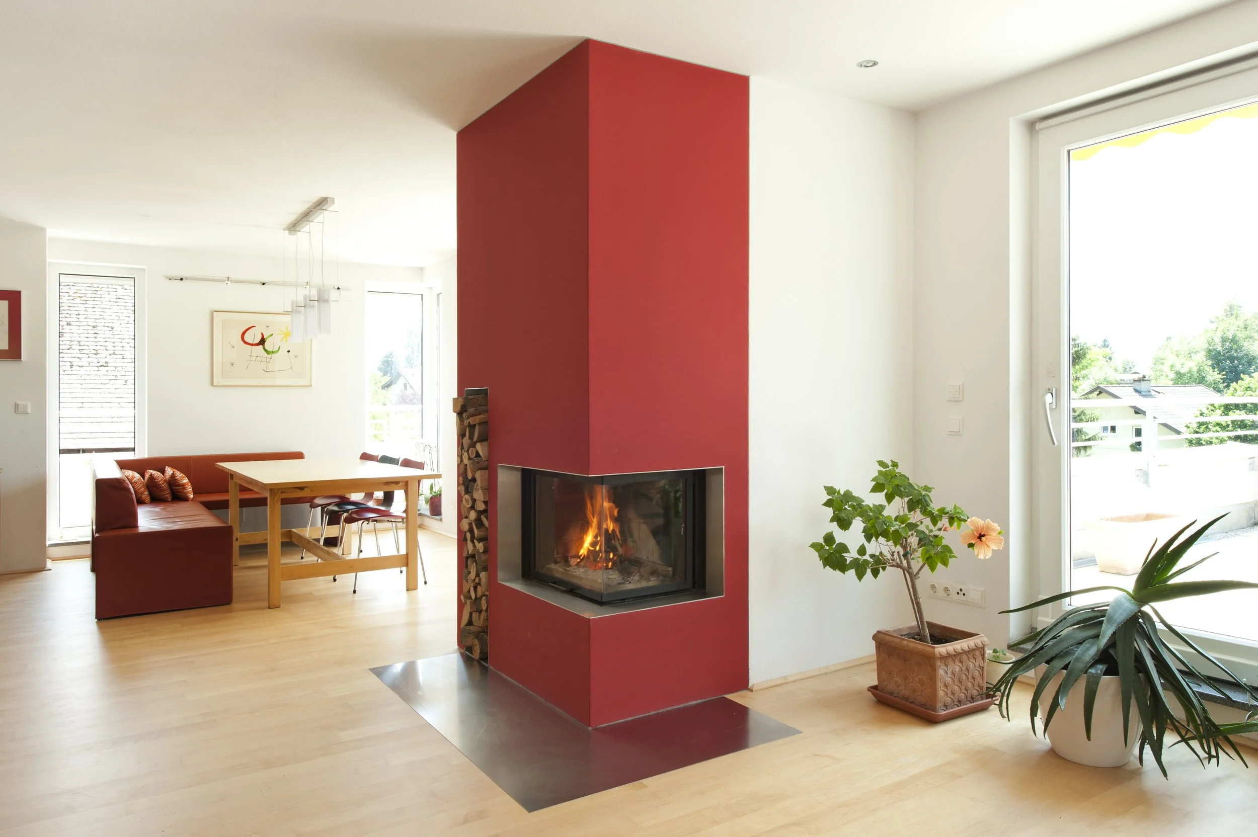 Großzügiger Kaminofen in rot gehalten mit natürlichem Licht durch große Fensterflächen.