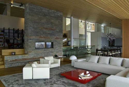 Moderner Wohnzimmerbereich mit weißen Sofas, einem roten Couchtisch, einem Kamin und großem Fenster in einer stilvollen, gut beleuchteten Wohnung.