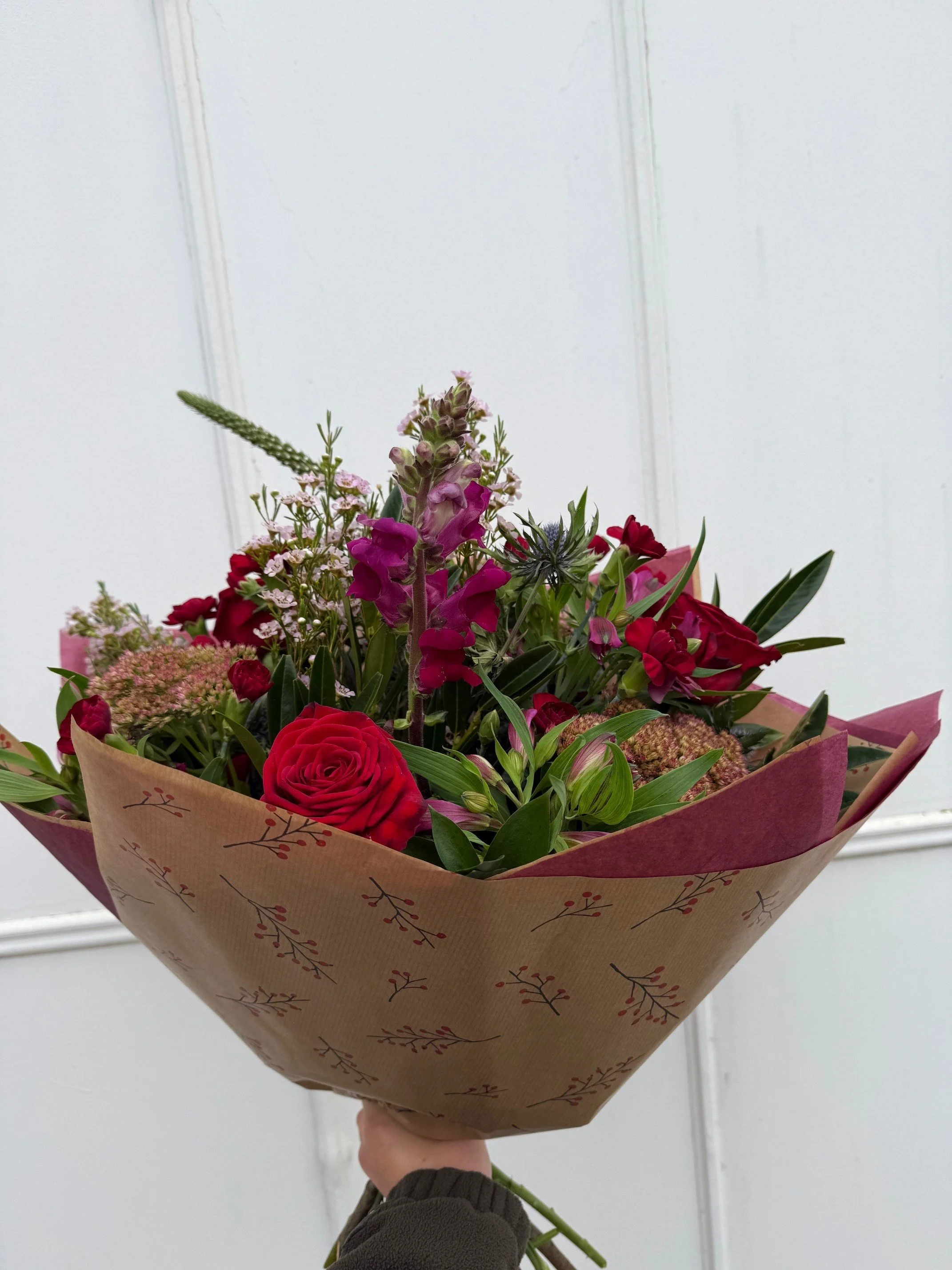 A bouquet of mixed flowers in a glass vase on a white surface.