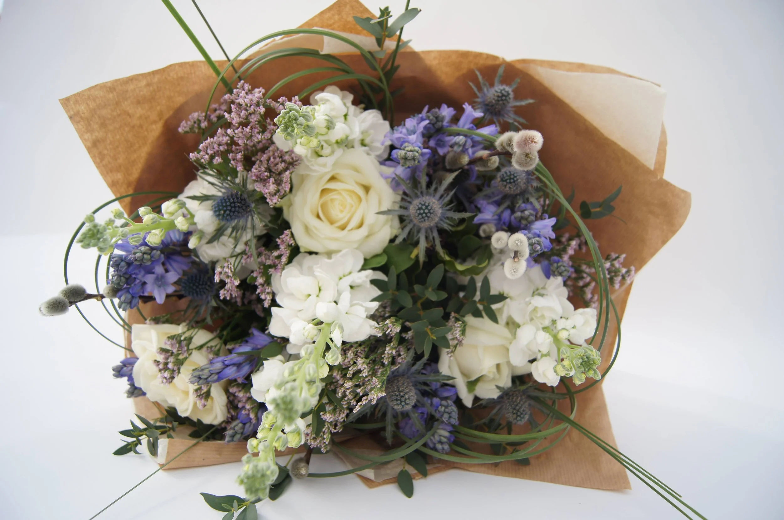A bouquet of mixed flowers in a glass vase on a white surface.
