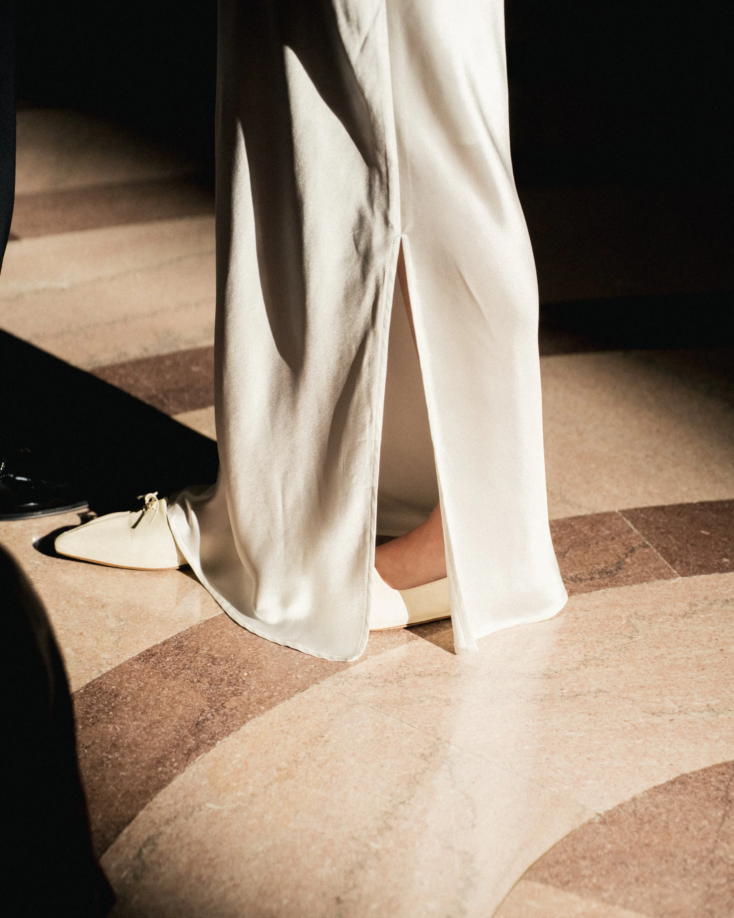 Close-up of a person wearing silky, cream-colored pants with a slit at the back, standing on a patterned tile floor.