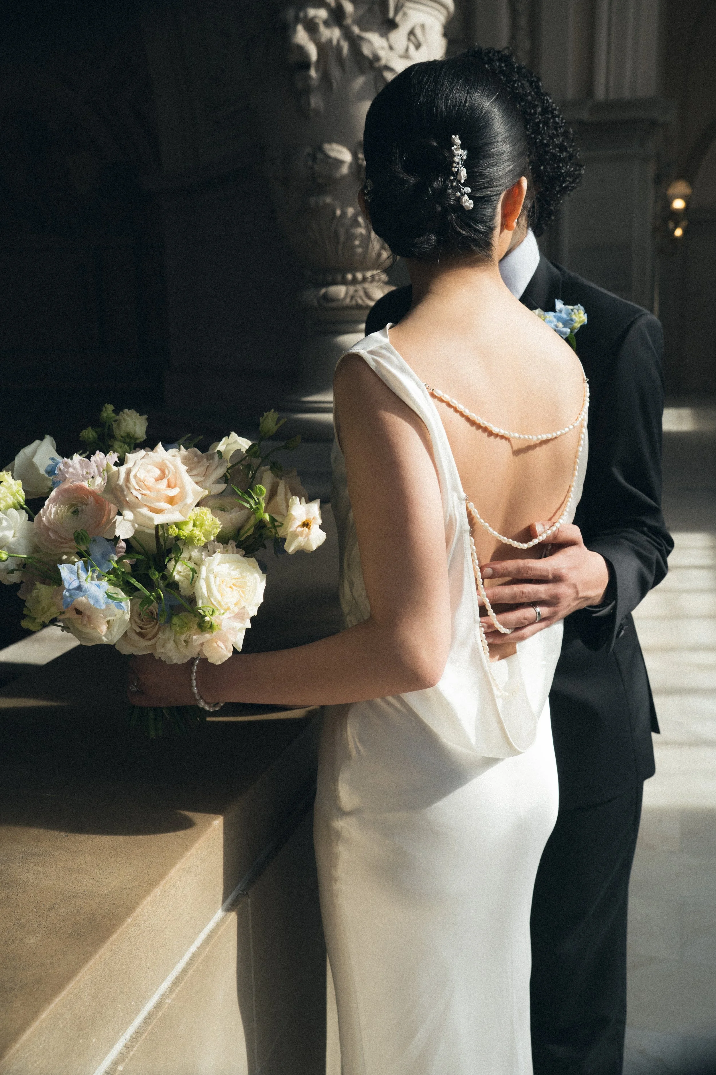 A bride in a white wedding dress holding a bouquet of flowers, standing close to a groom in a black suit at a wedding ceremony.