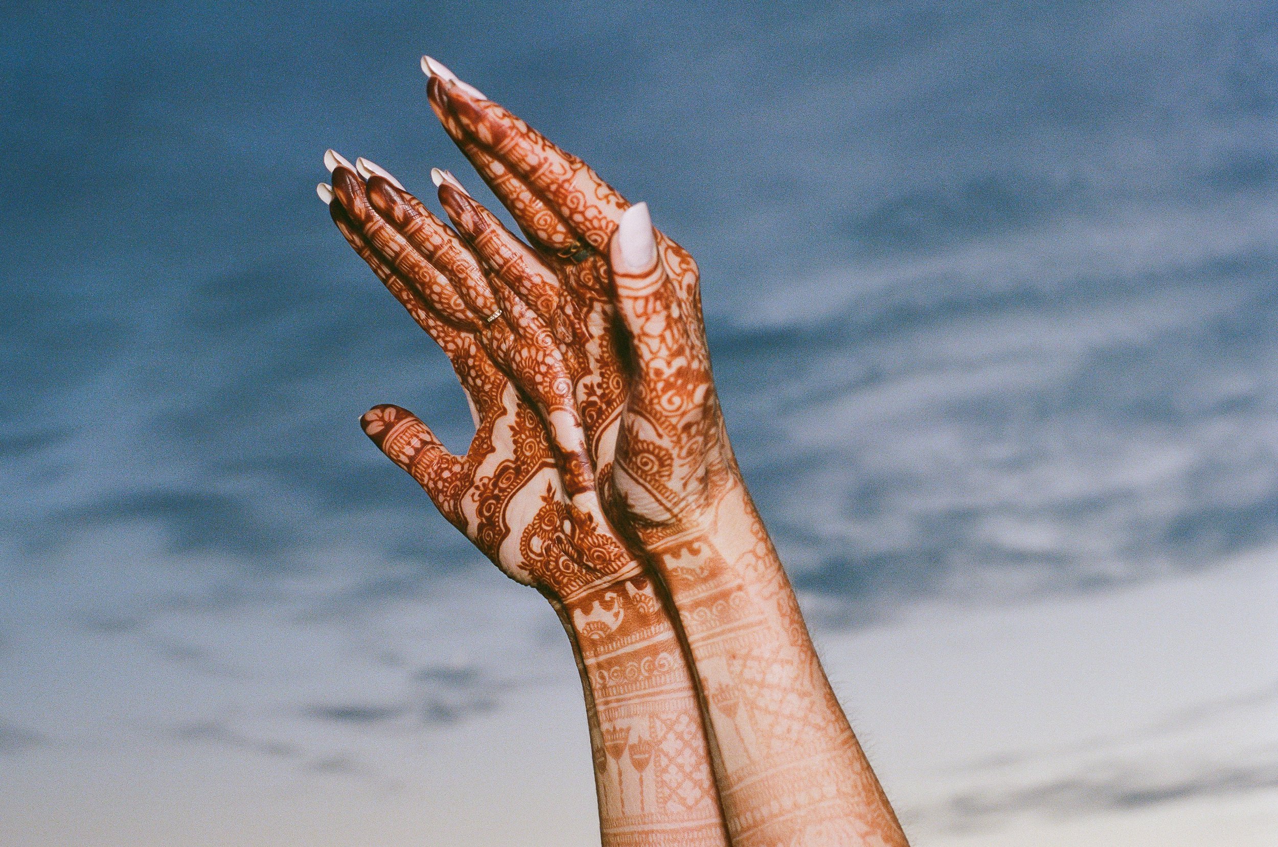 Two hands with intricate henna designs are raised against a cloudy sky.